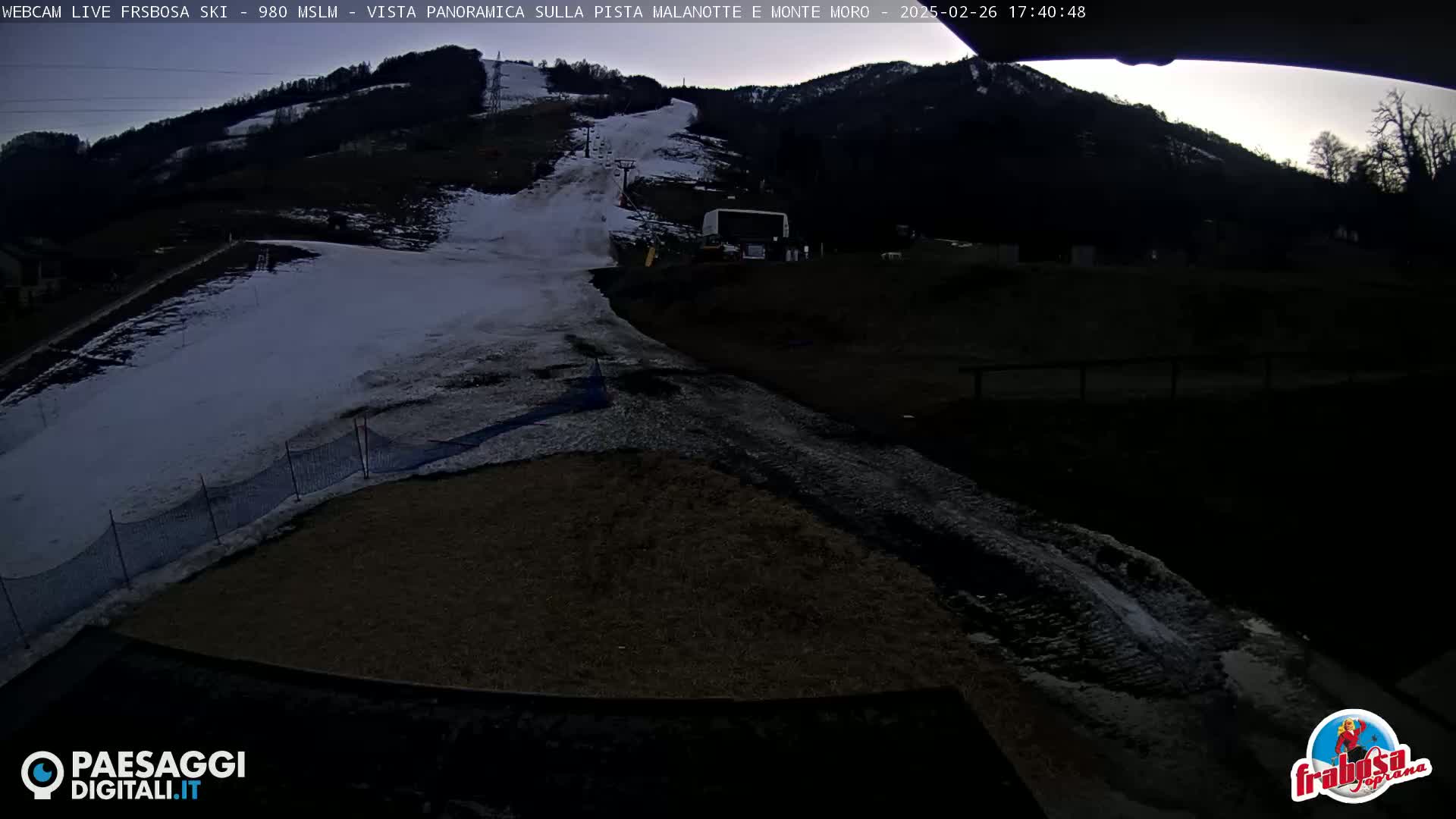 A snow-covered ski slope is visible at dusk, with a partially snow-covered area at the bottom of the hill.