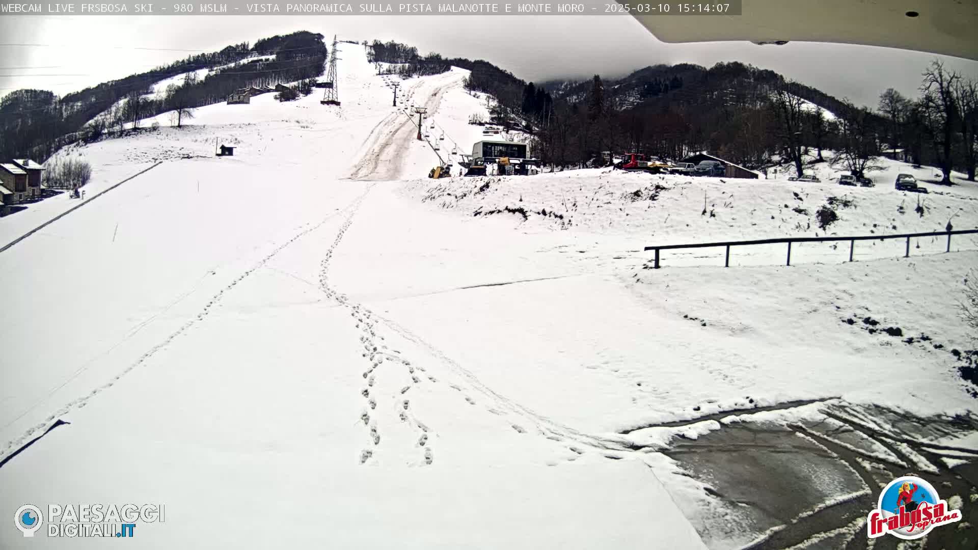 A snow-covered ski slope with a ski lift and several footprints in the snow, under an overcast sky.
