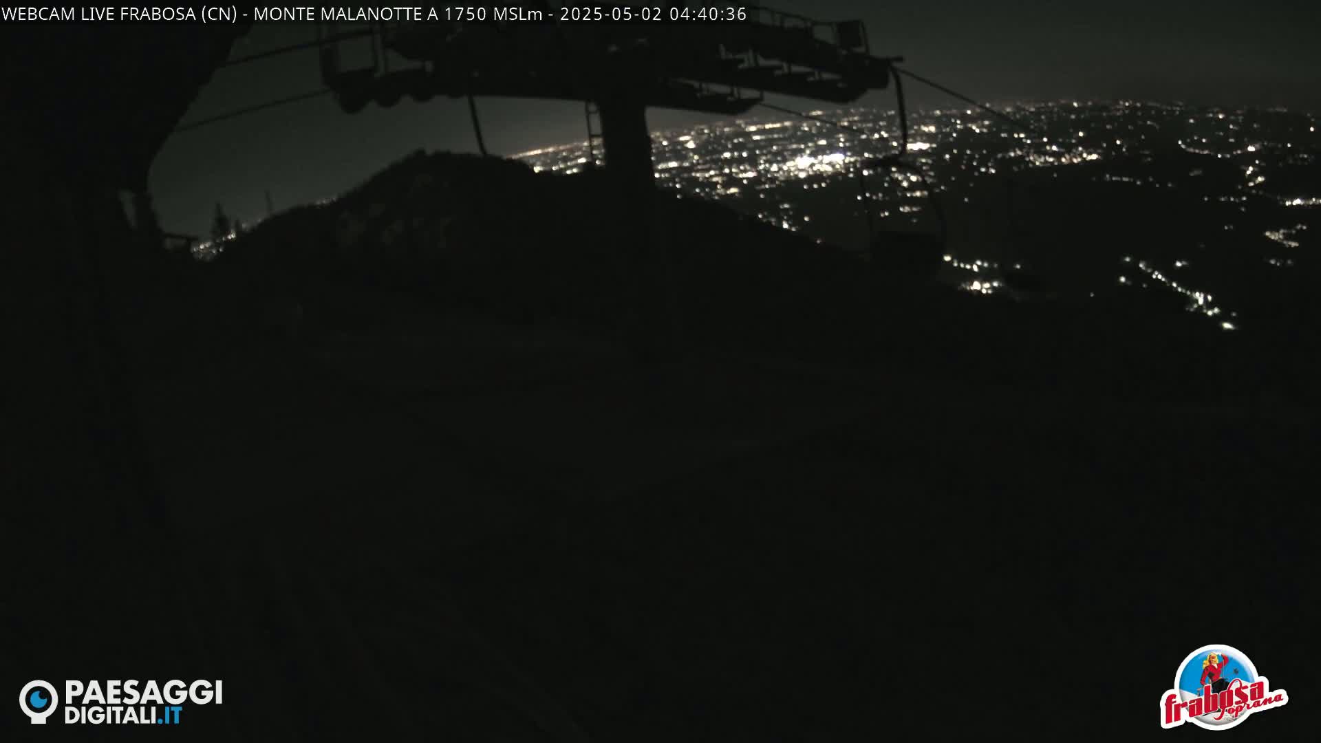 A nighttime view from a ski lift shows a distant city illuminated below, under a clear, dark sky.