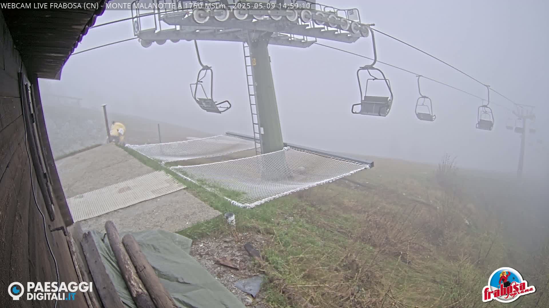 A foggy mountaintop scene shows a chairlift, empty chairs, and two hammocks near a building, with a person in yellow standing near the bottom of the lift.