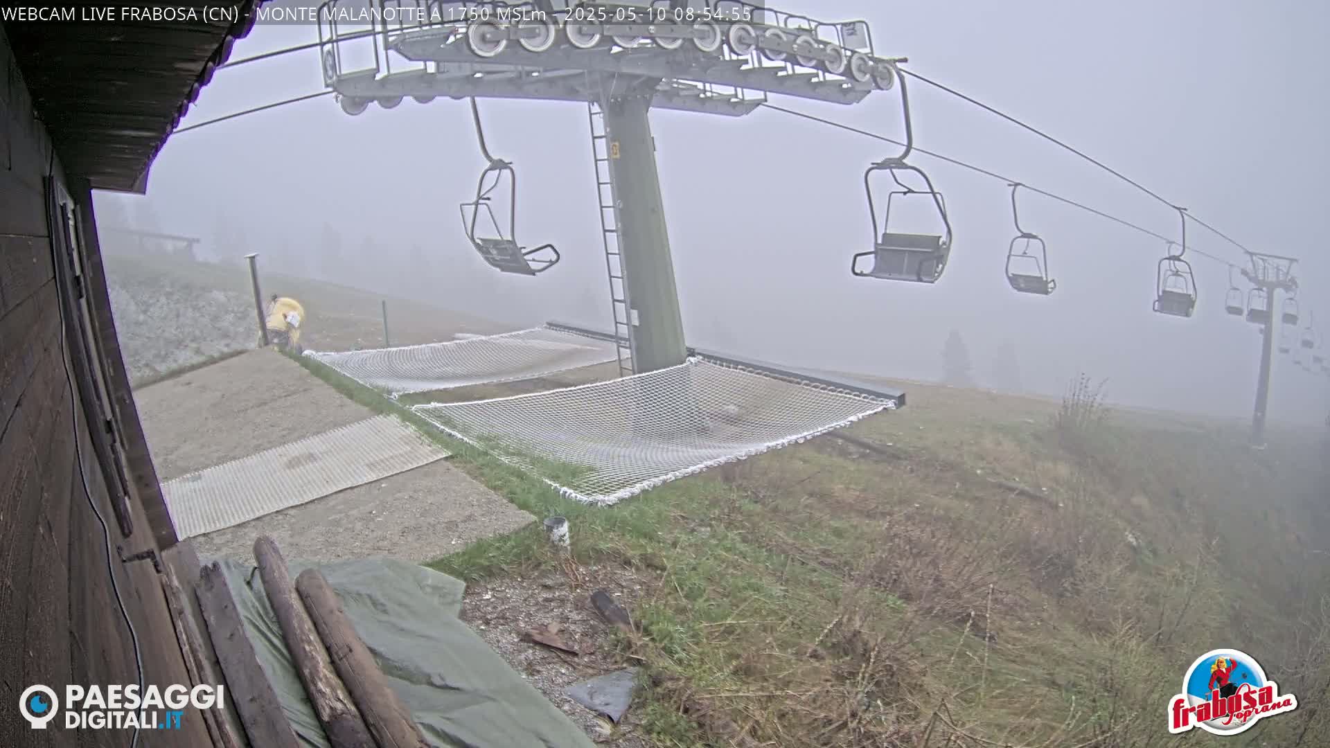 A chairlift sits in foggy conditions above two empty mesh hammocks near a grassy hillside.