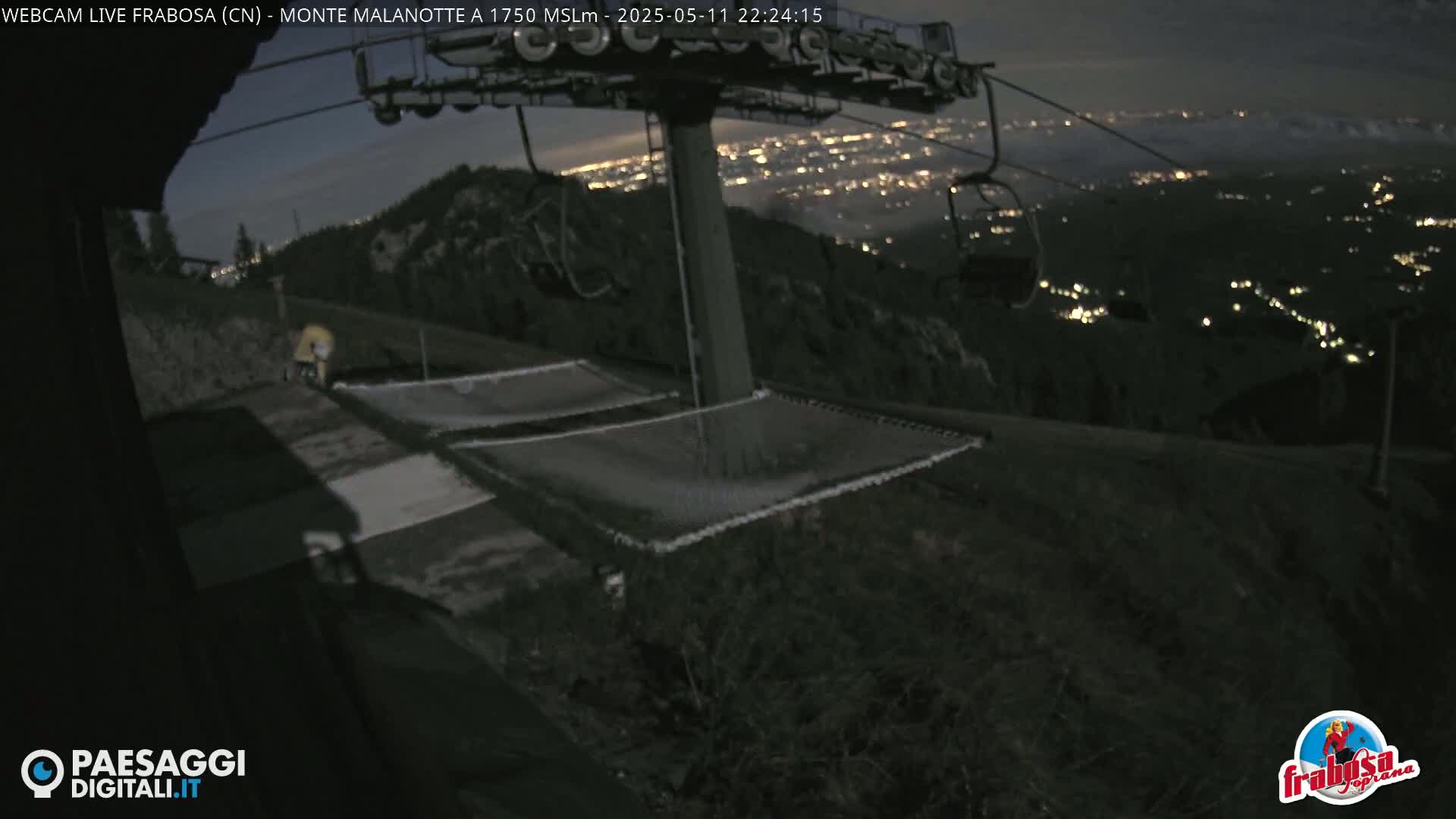 At night, a mountaintop ski lift overlooks a valley illuminated by distant city lights.