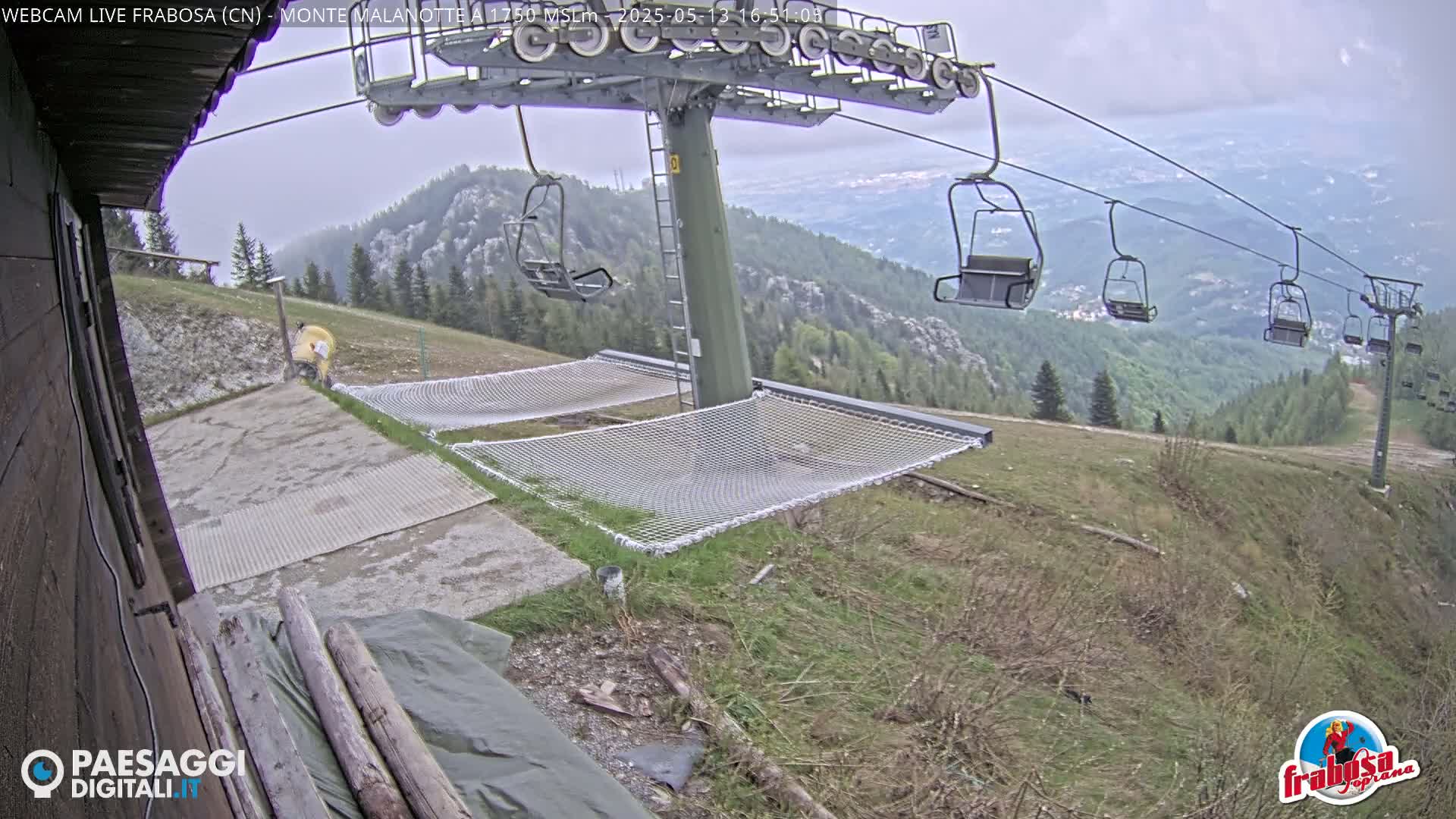 A chairlift overlooks a grassy mountainside with empty chairs and safety nets on an overcast day.