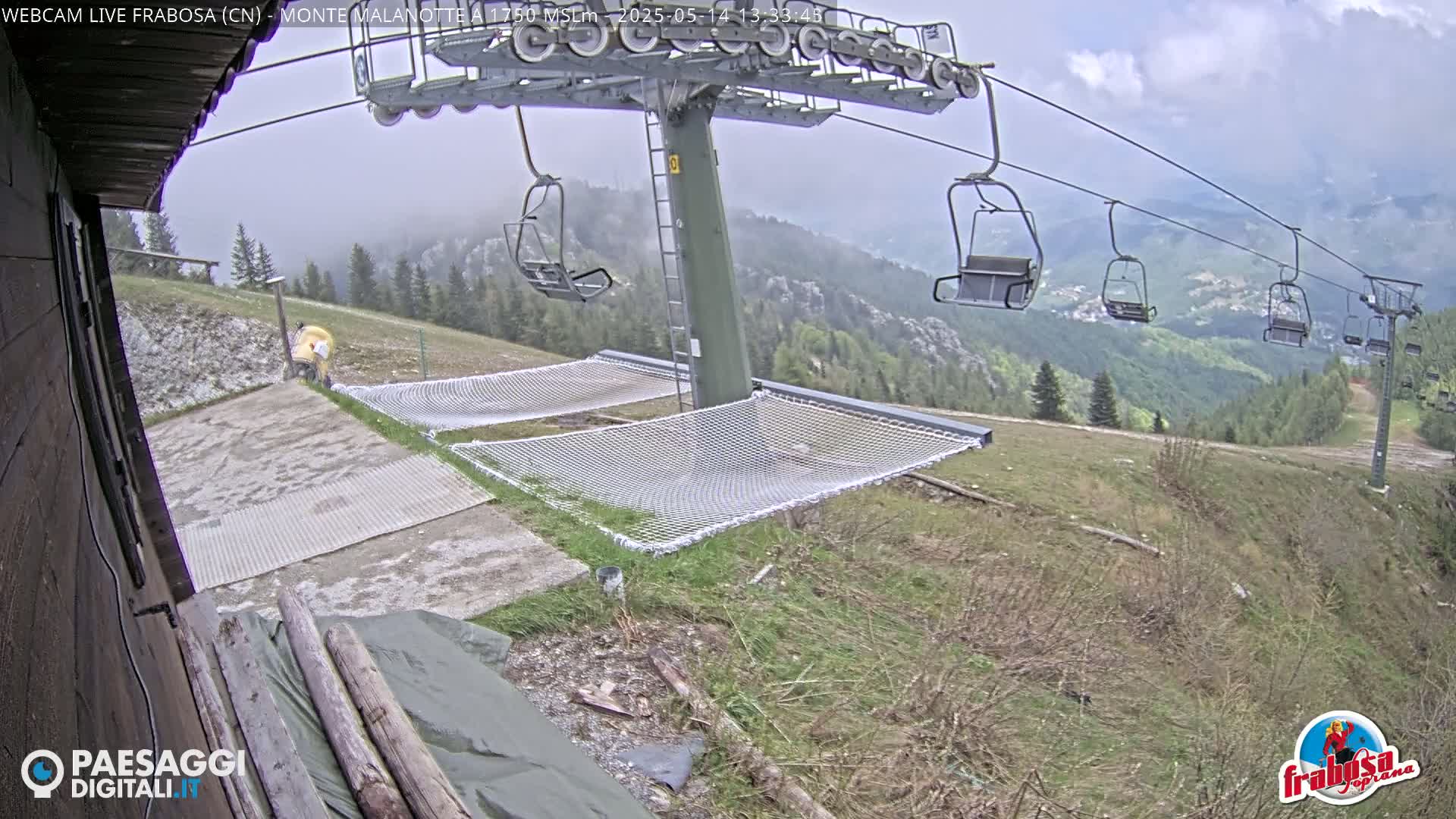 A chairlift with empty chairs overlooks a grassy hillside on an overcast day, with several nets for lounging at the base of the lift.