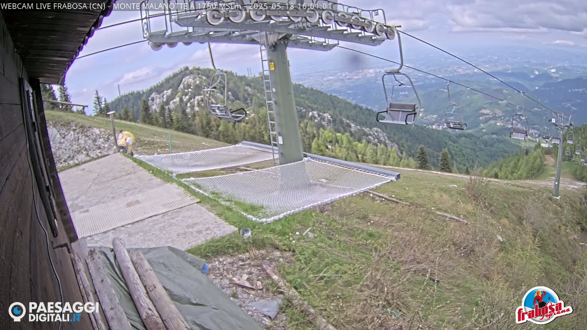 A mountaintop view shows a chairlift, empty hammocks, and a person near a building under a partly cloudy sky.