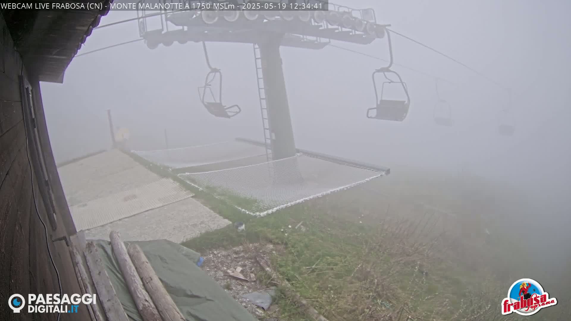 A chairlift ascends into a thick fog, with a hammock and a paved area visible below.