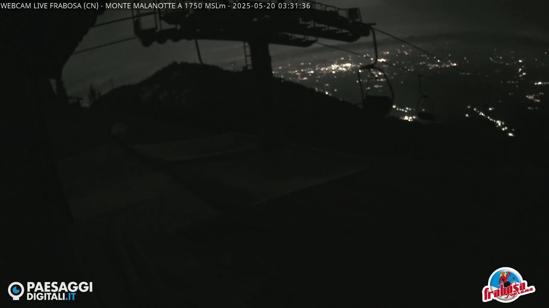 A nighttime view from a chairlift shows a distant city glowing with lights under a dark sky.