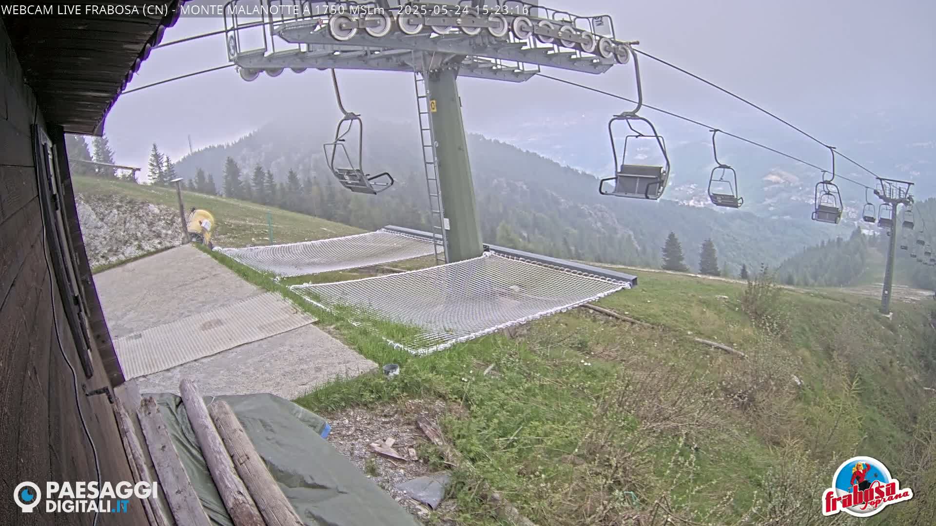 A chairlift ascends a hazy mountainside, with two empty safety nets at the base on a partly cloudy day.
