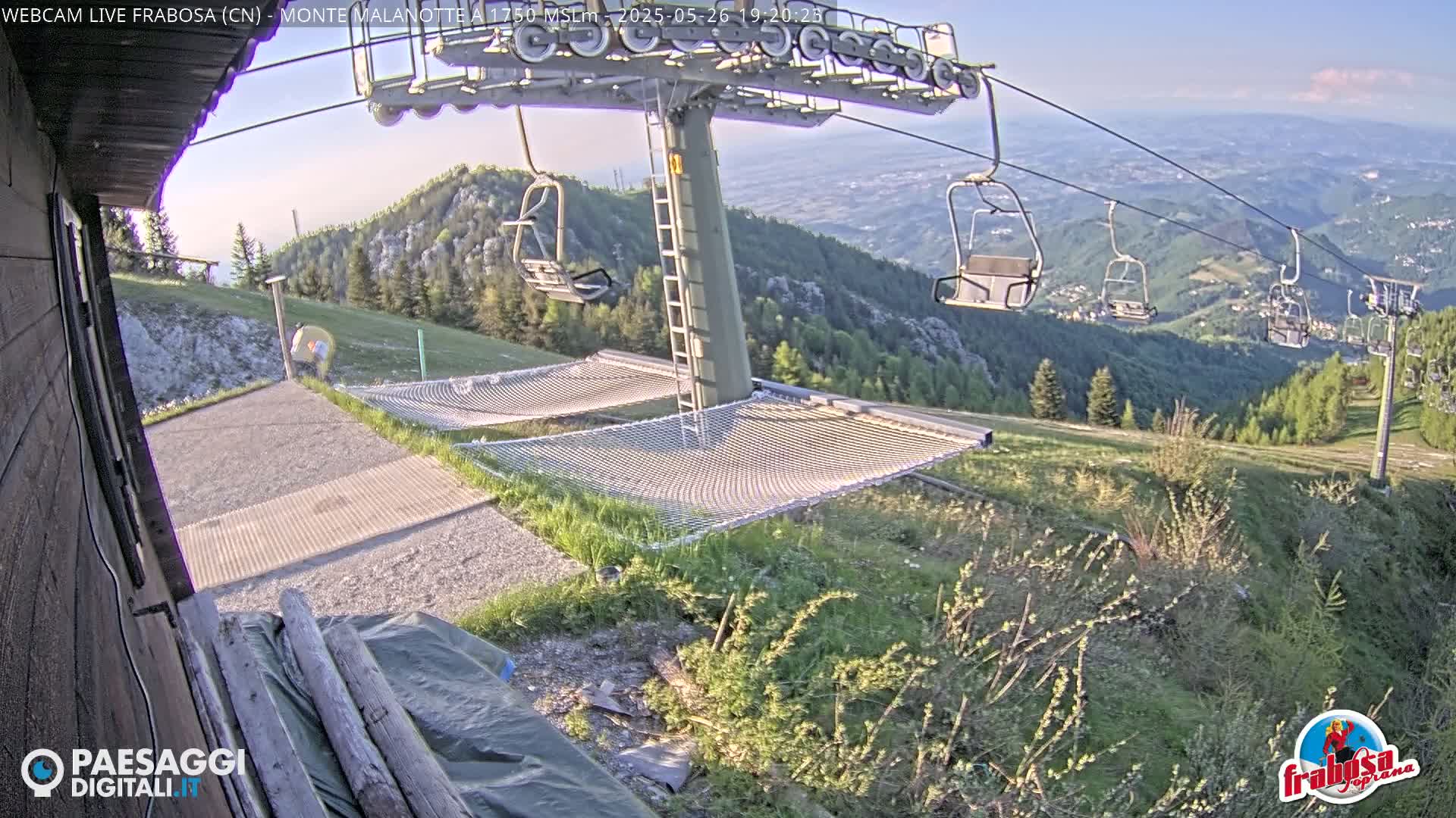 A mountaintop view shows a chairlift, empty hammocks, and a grassy hillside under a clear evening sky.