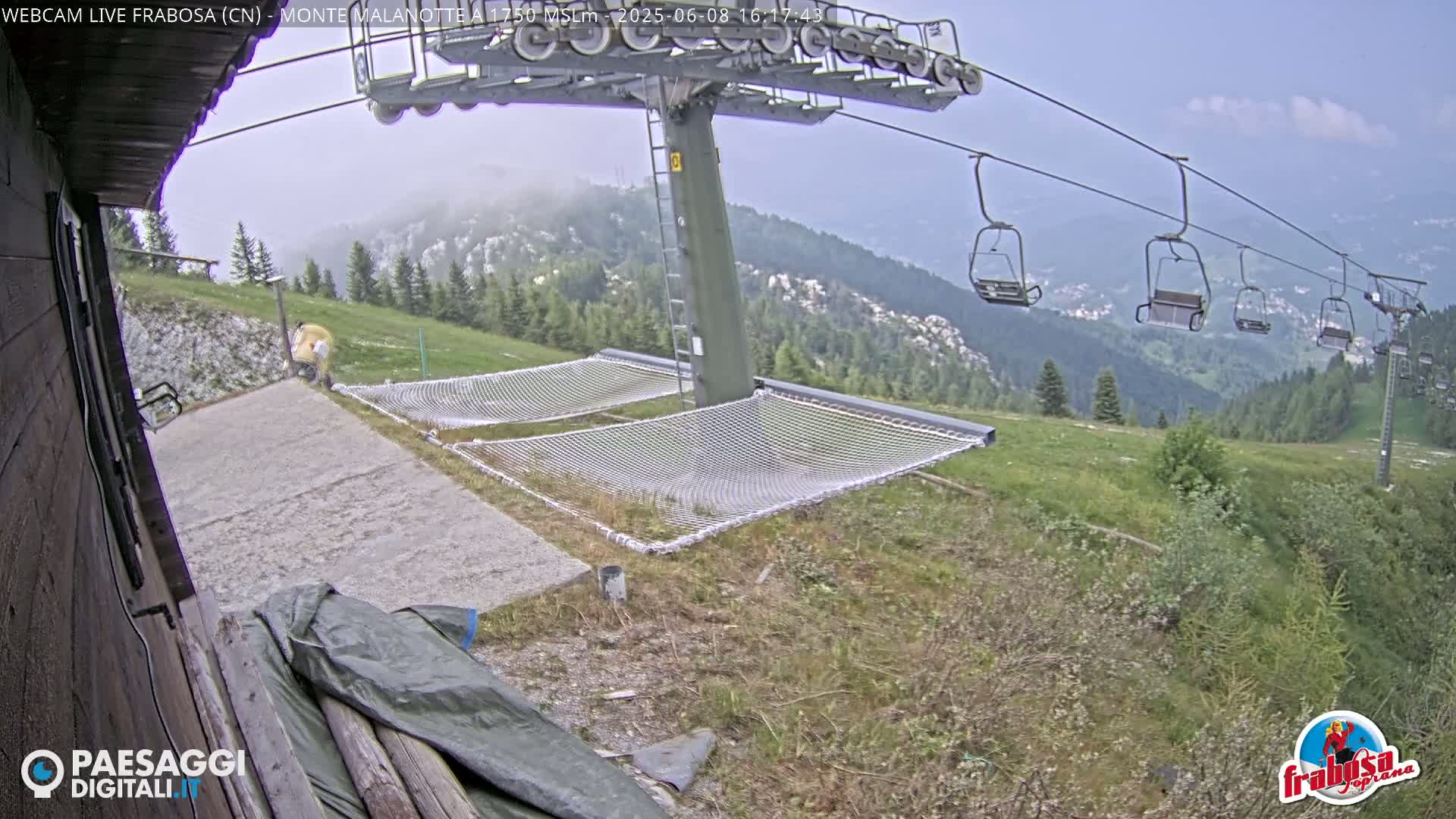 Two empty mesh hammocks sit near a chairlift on a grassy mountainside under a hazy sky.