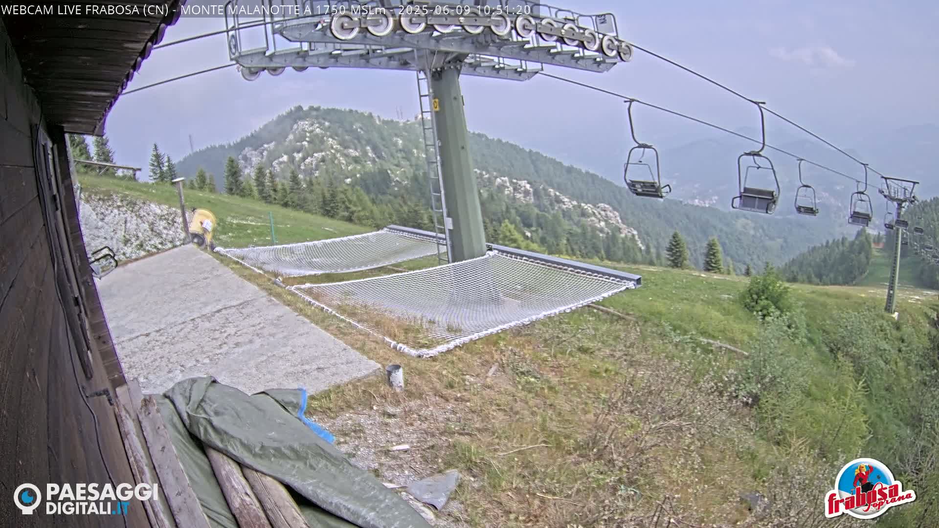A chairlift ascends a mountain on an overcast day, overlooking a grassy area with several empty nets and a paved surface.