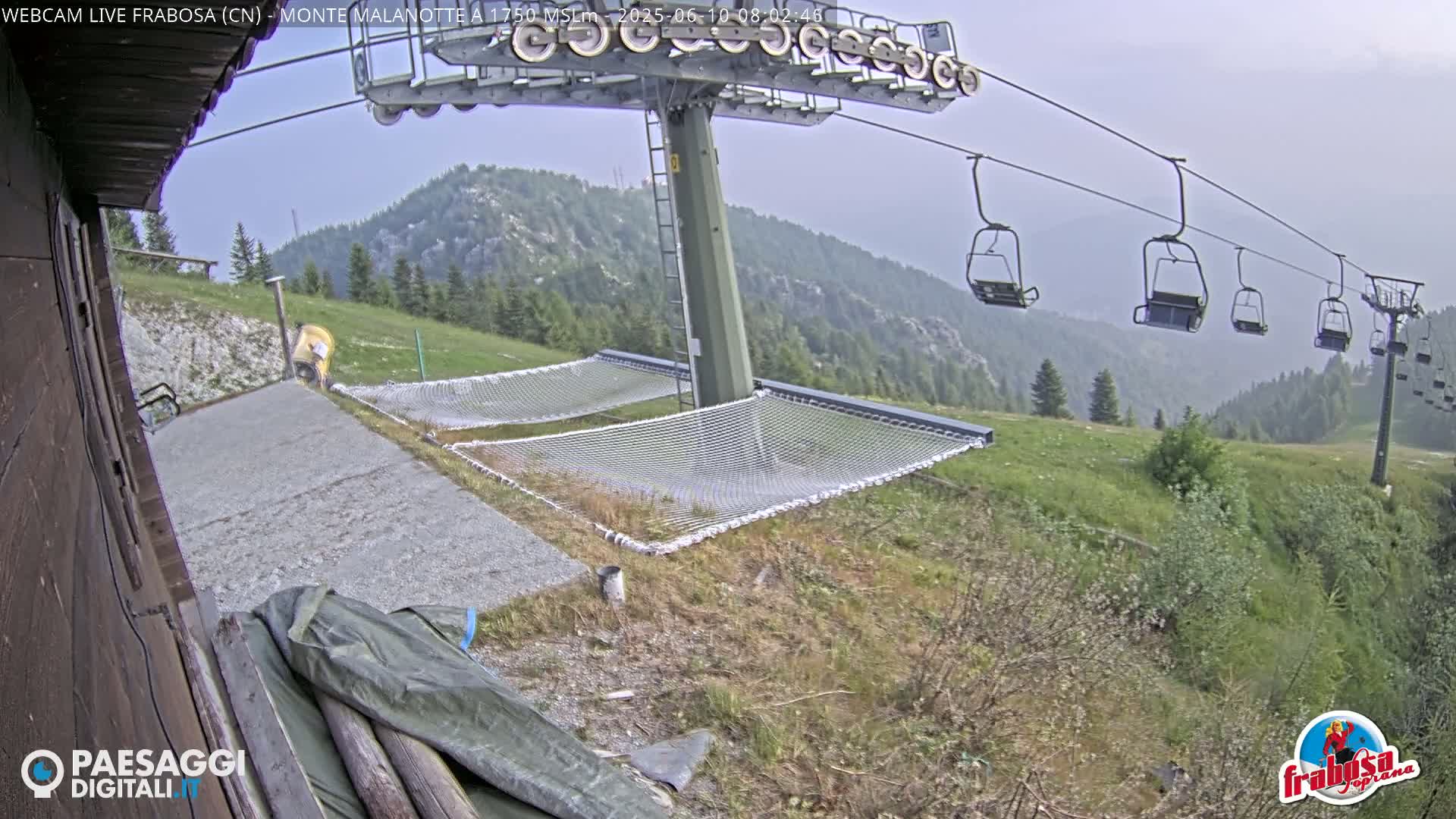 A chairlift with empty chairs overlooks a grassy hillside with two empty nets near a building under an overcast sky.