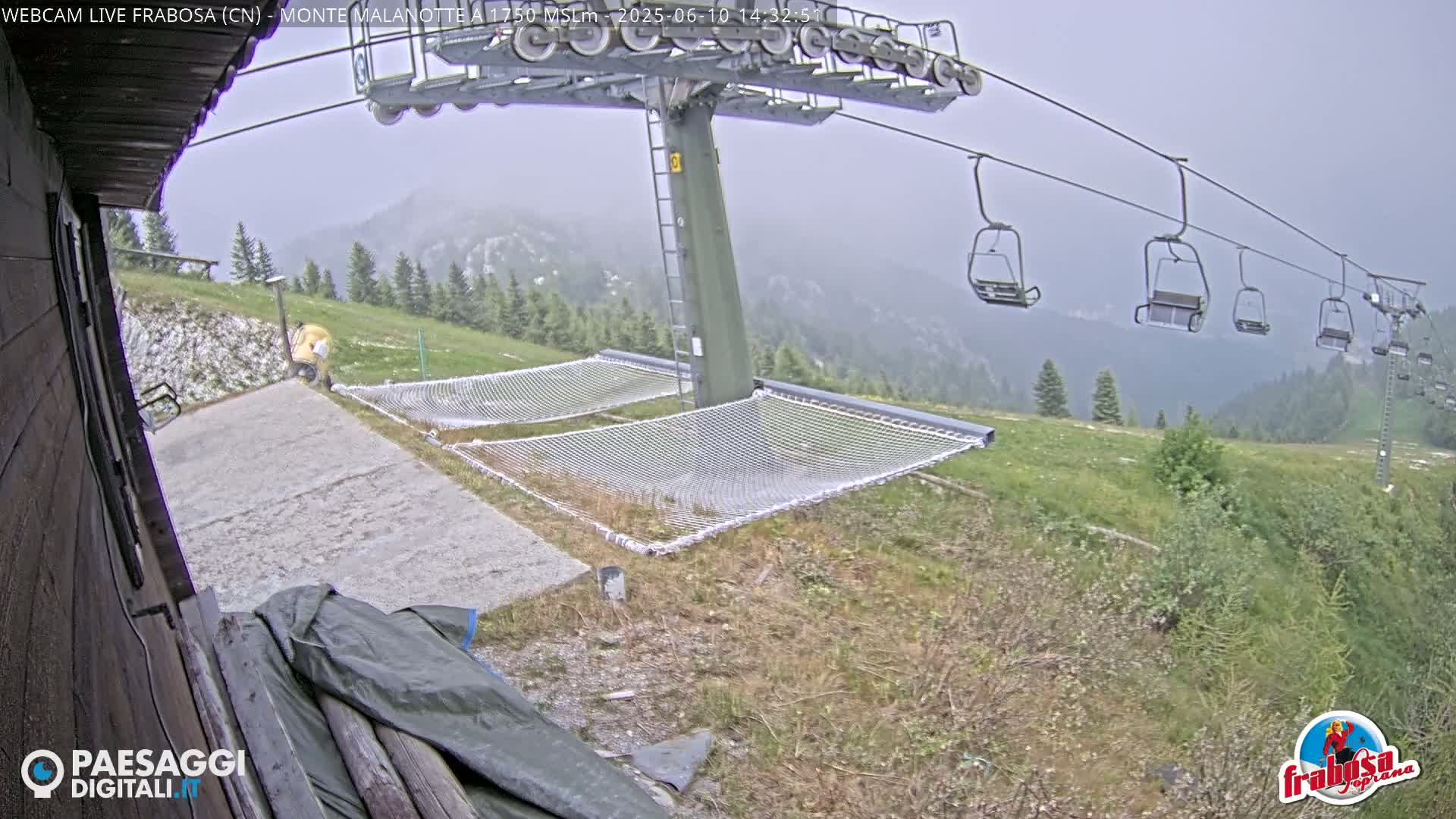 A chairlift and empty nets sit on a grassy mountainside in hazy weather.
