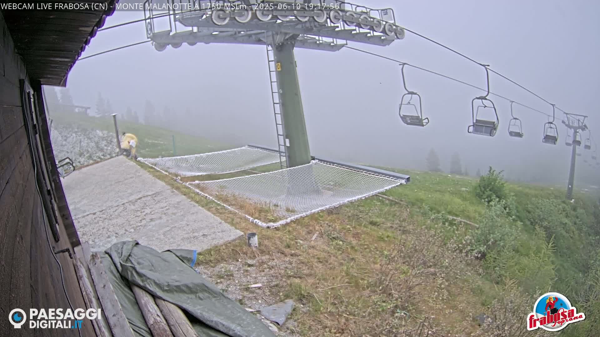 A foggy mountaintop scene shows a chairlift with empty chairs, two empty mesh hammocks, and a person standing near a concrete area.
