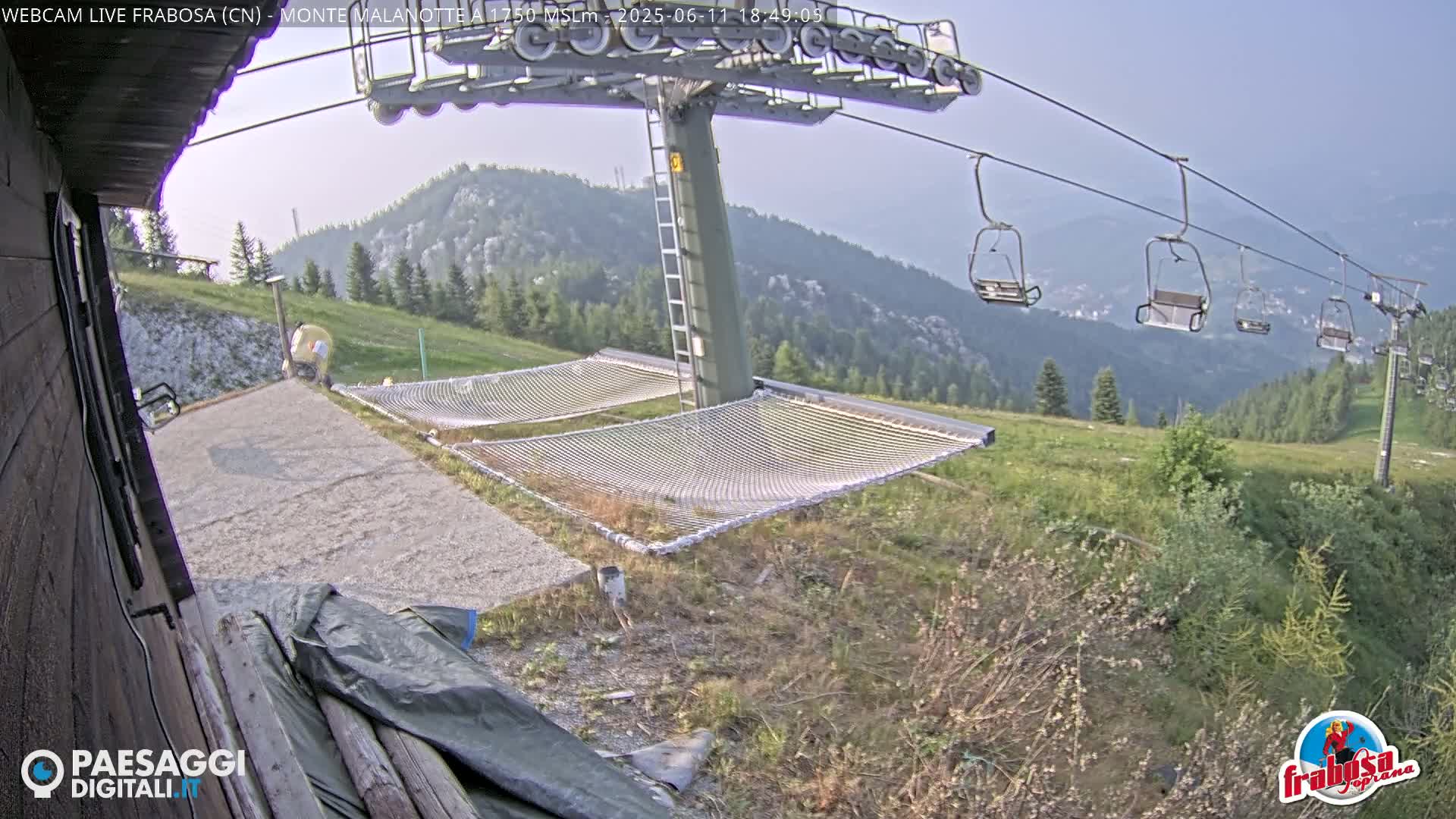 A mountaintop view shows a chairlift with empty chairs, two empty mesh hammocks on a gravel area, and a hazy, clear sky.