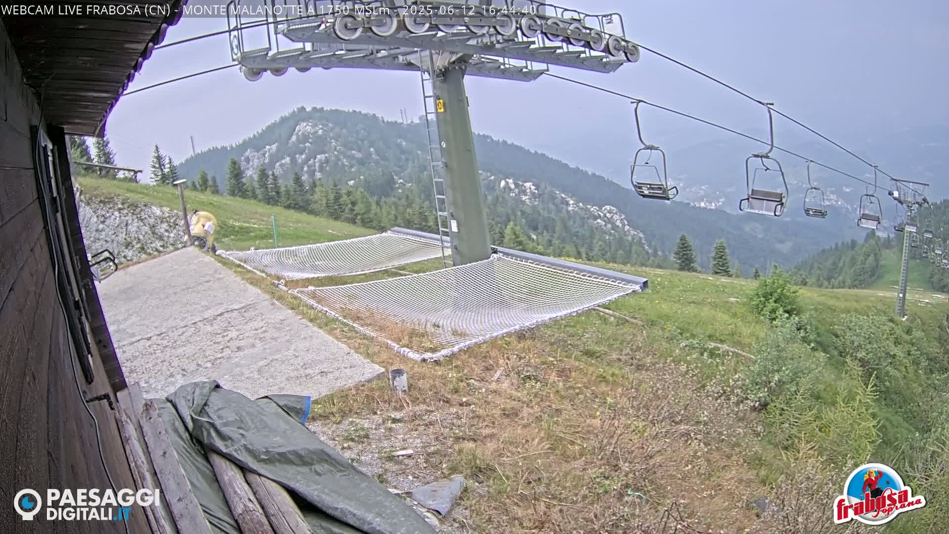 A chairlift ascends a mountain on an overcast day, with two empty nets spread out on the grassy ground below.