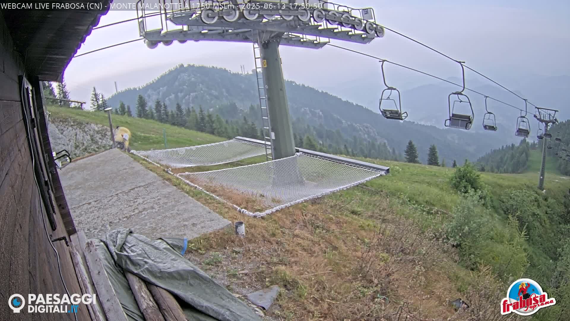 A chairlift with empty chairs overlooks a grassy hillside with two empty net hammocks near a concrete pad under an overcast sky.
