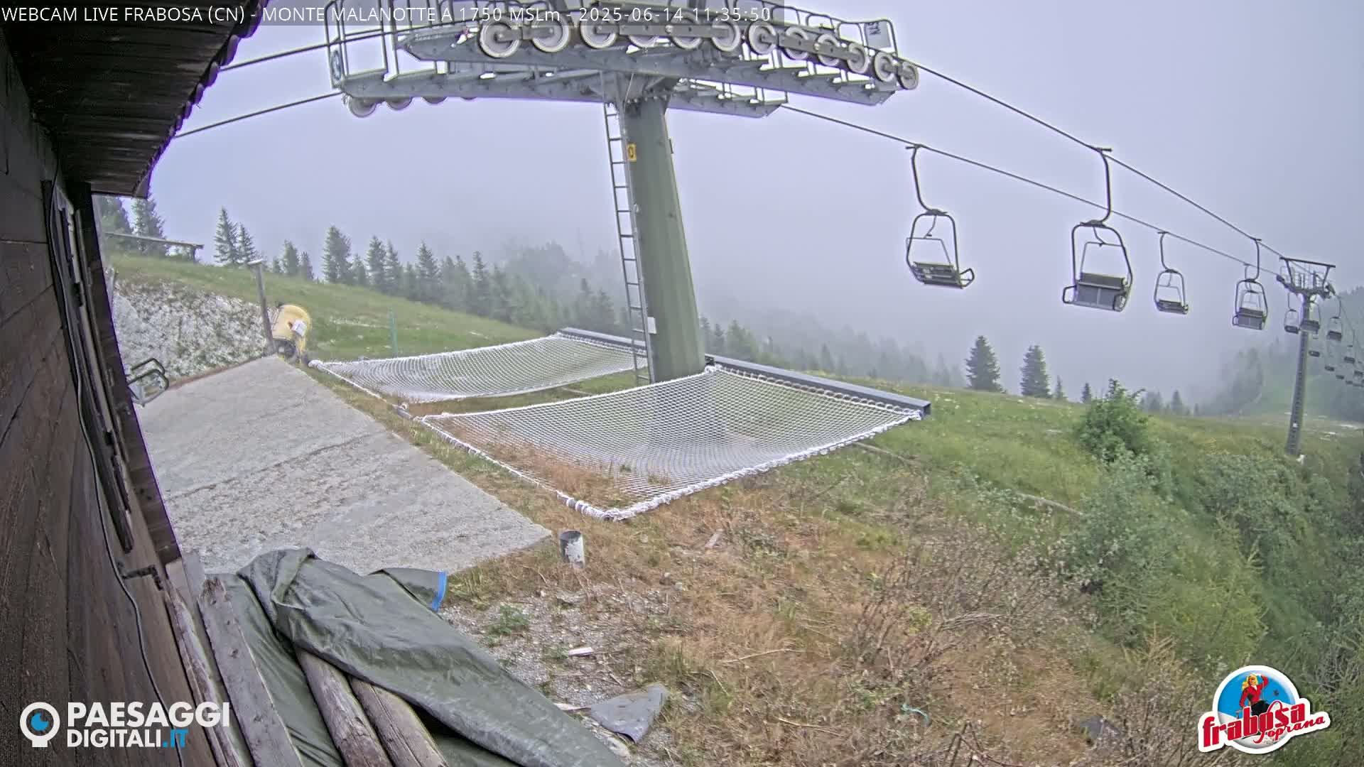 A chairlift with empty chairs overlooks a grassy hillside with two safety nets on a misty day.