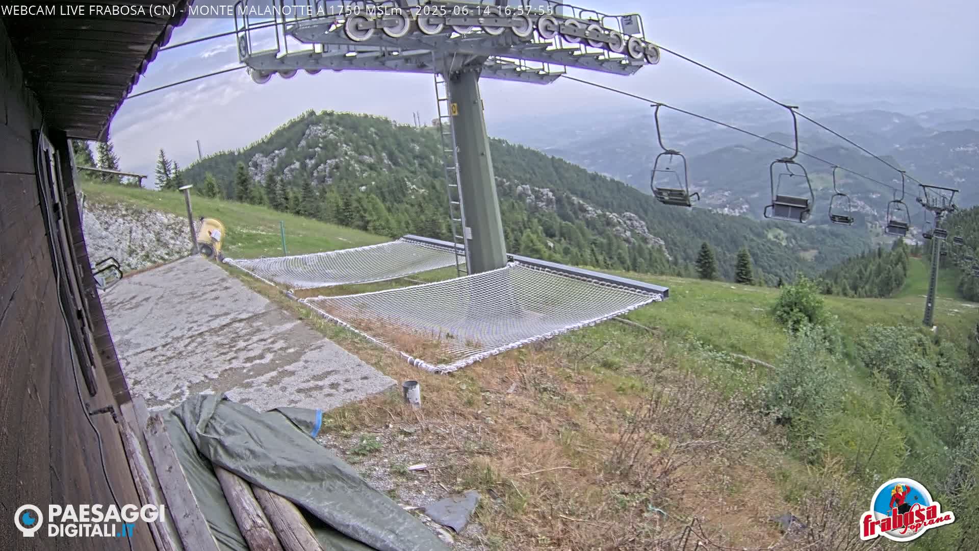 A mountaintop view shows an overcast sky, a chairlift, and two empty net hammocks near a building.