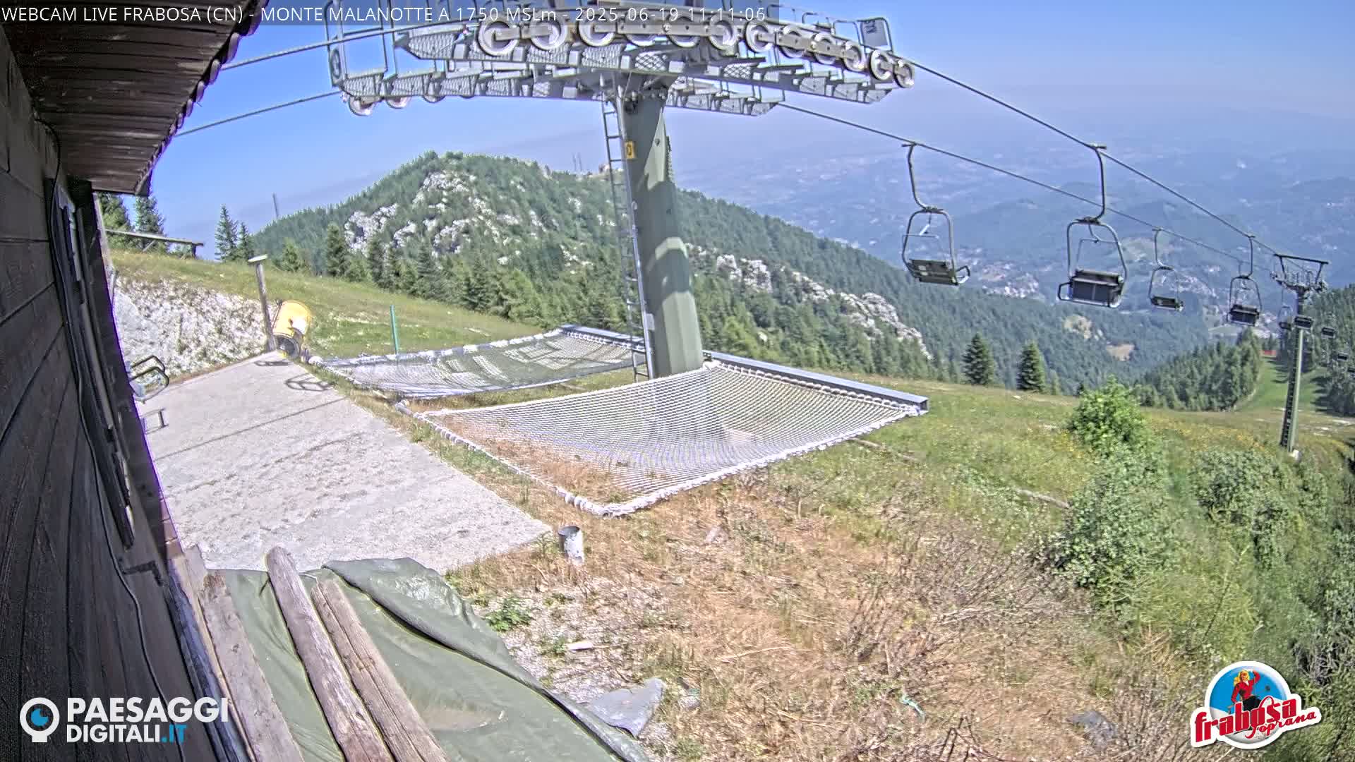 A mountaintop view on a clear, sunny day shows a chairlift, several empty chairlift seats, and several large nets laid out on the ground.