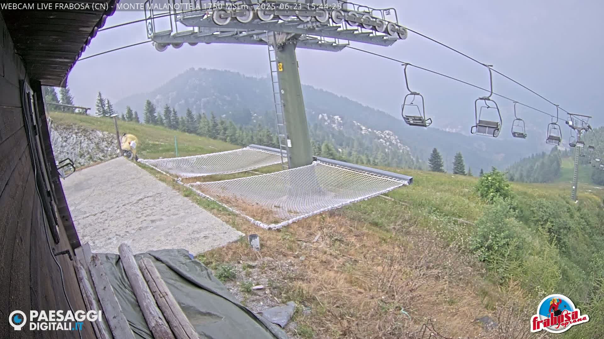 A chairlift ascends a mountain on an overcast day, with two empty net hammocks situated below.