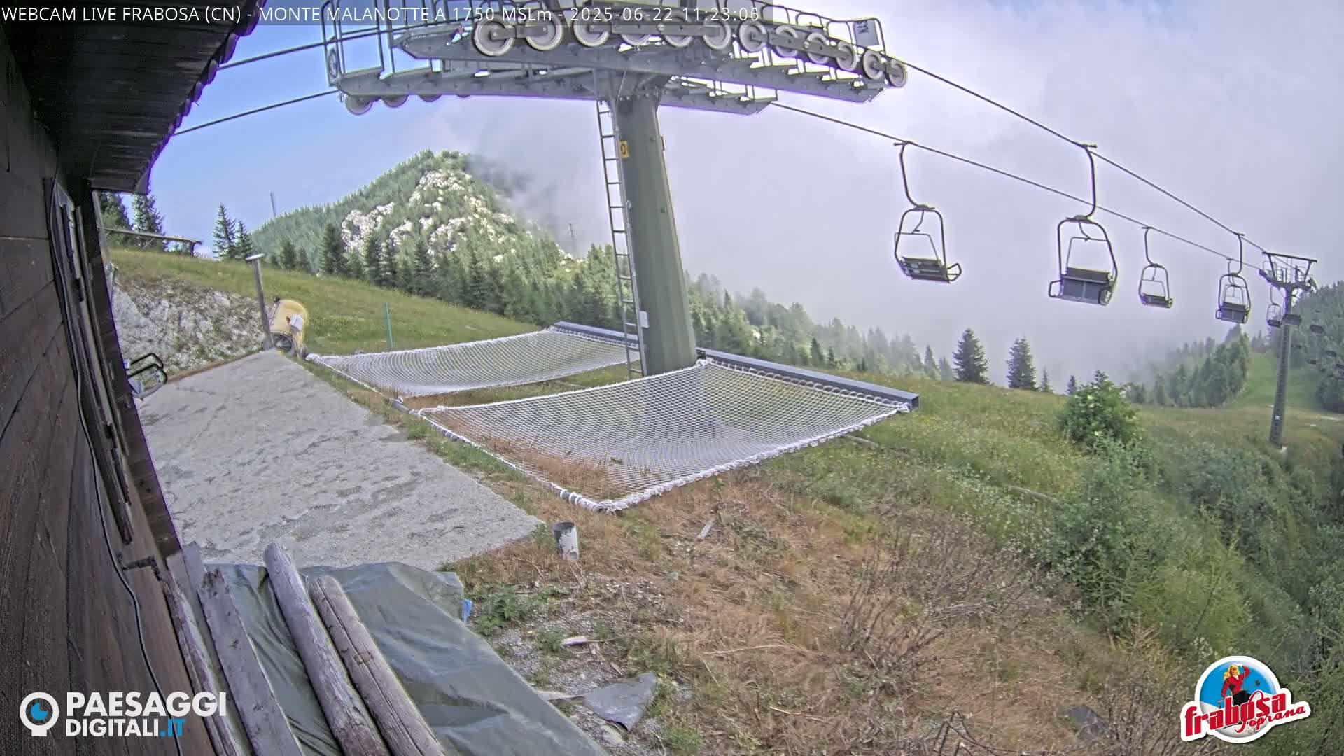 A chairlift ascends a mountainside on an overcast day, passing over grassy areas with several empty nets laid out on the ground.