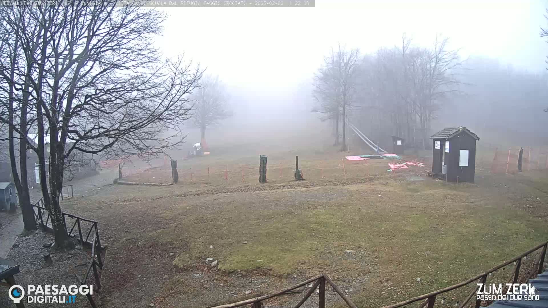 A foggy, outdoor scene shows a mostly barren, grassy area with leafless trees and a small shed, partially enclosed by fencing.