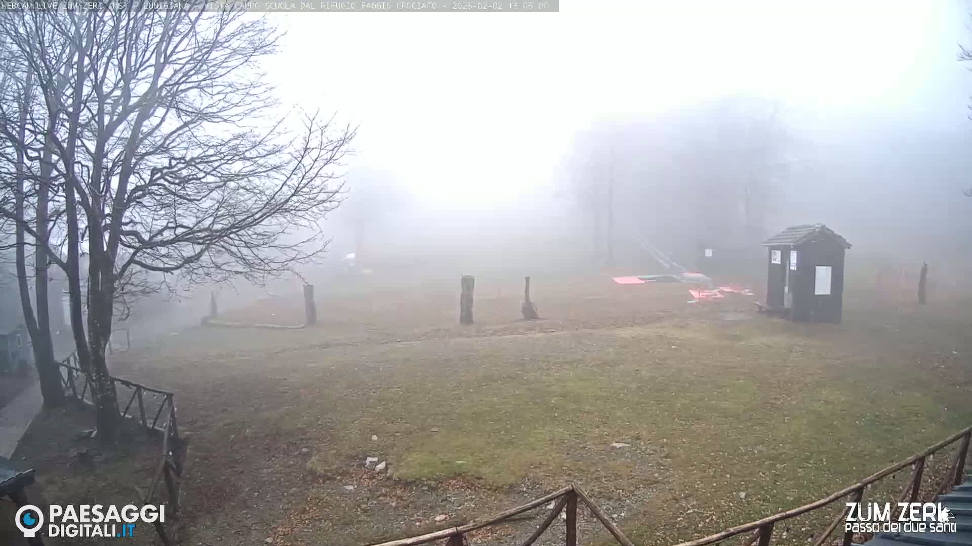 A foggy, open field with bare trees, a small building, and wooden posts is visible.