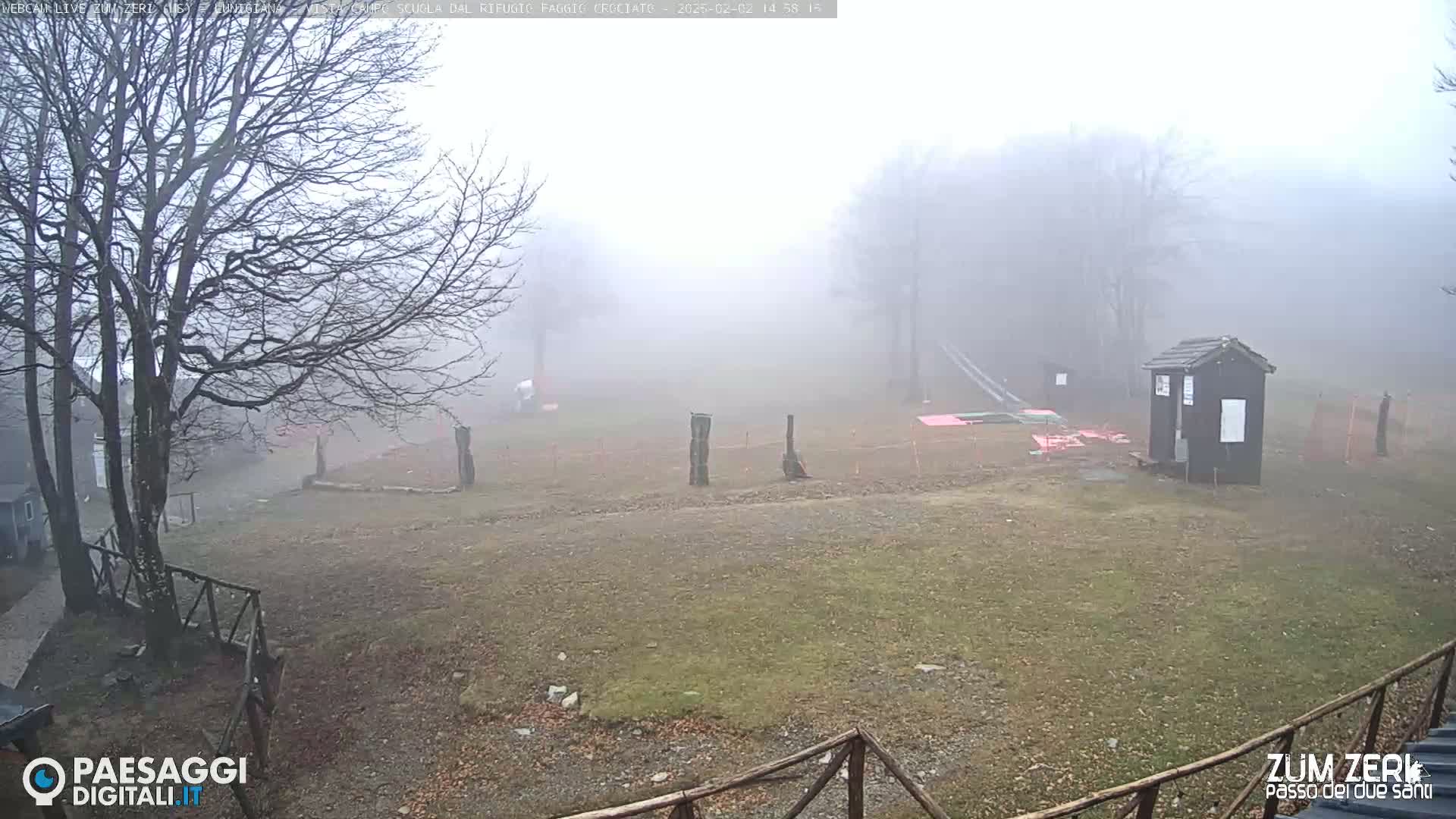 A foggy, outdoor scene shows a grassy area with a few structures, some fencing, and bare trees in the background.