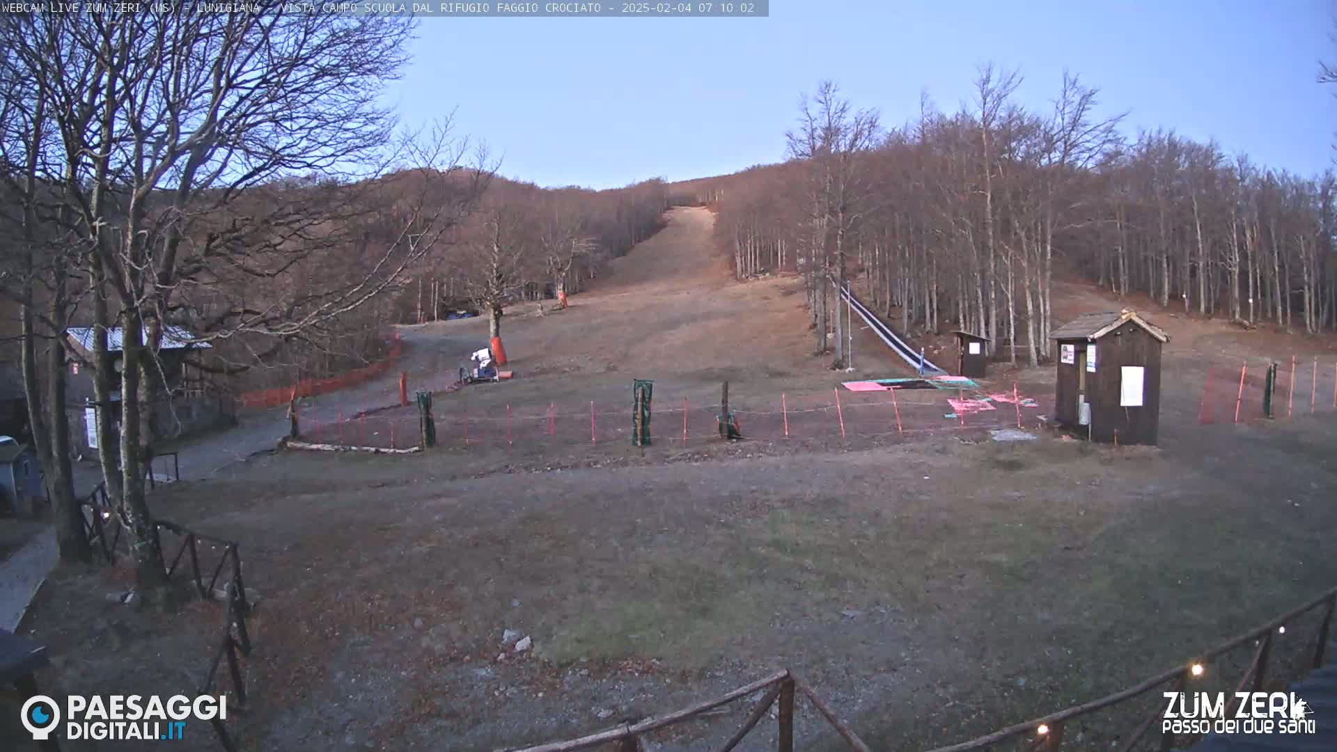 A mostly barren ski slope is surrounded by leafless trees under a clear, light-blue sky.