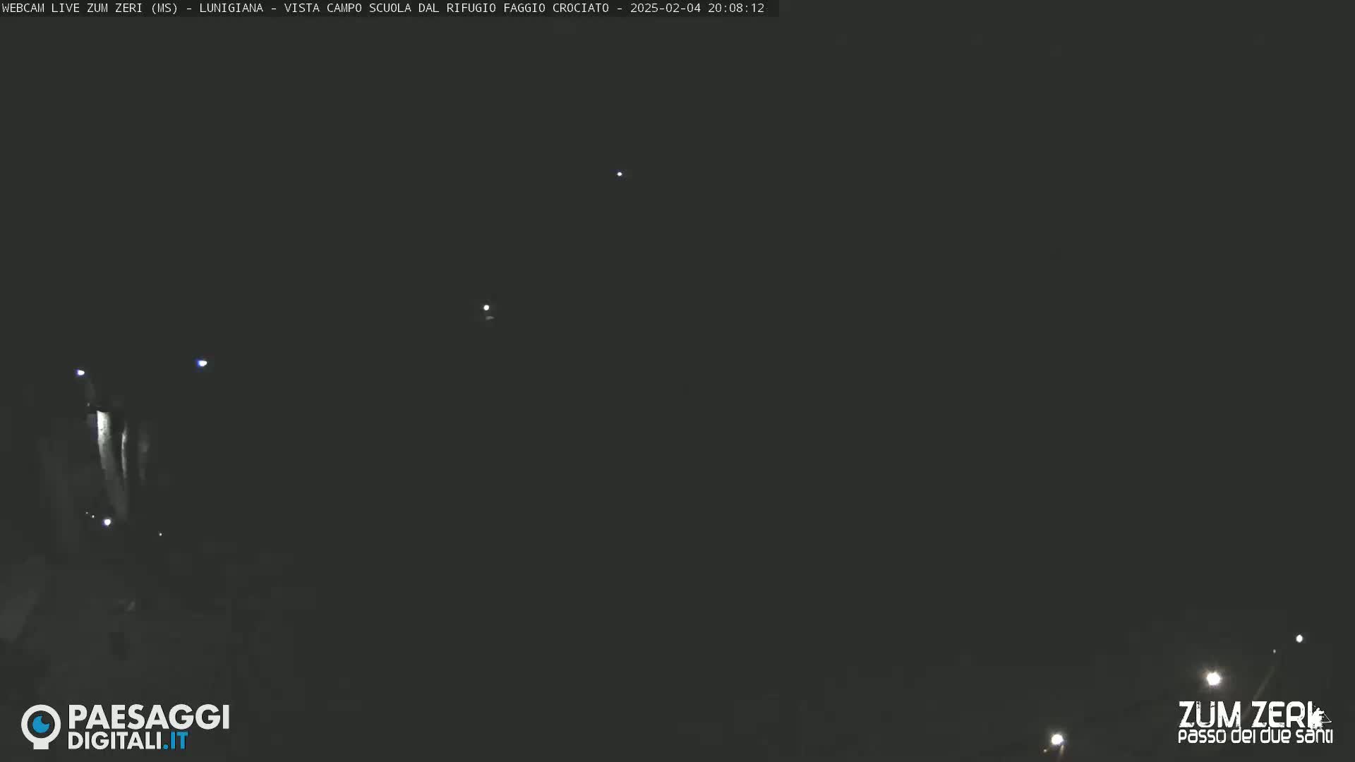 A dark, nighttime scene with a few faint lights visible in the distance.