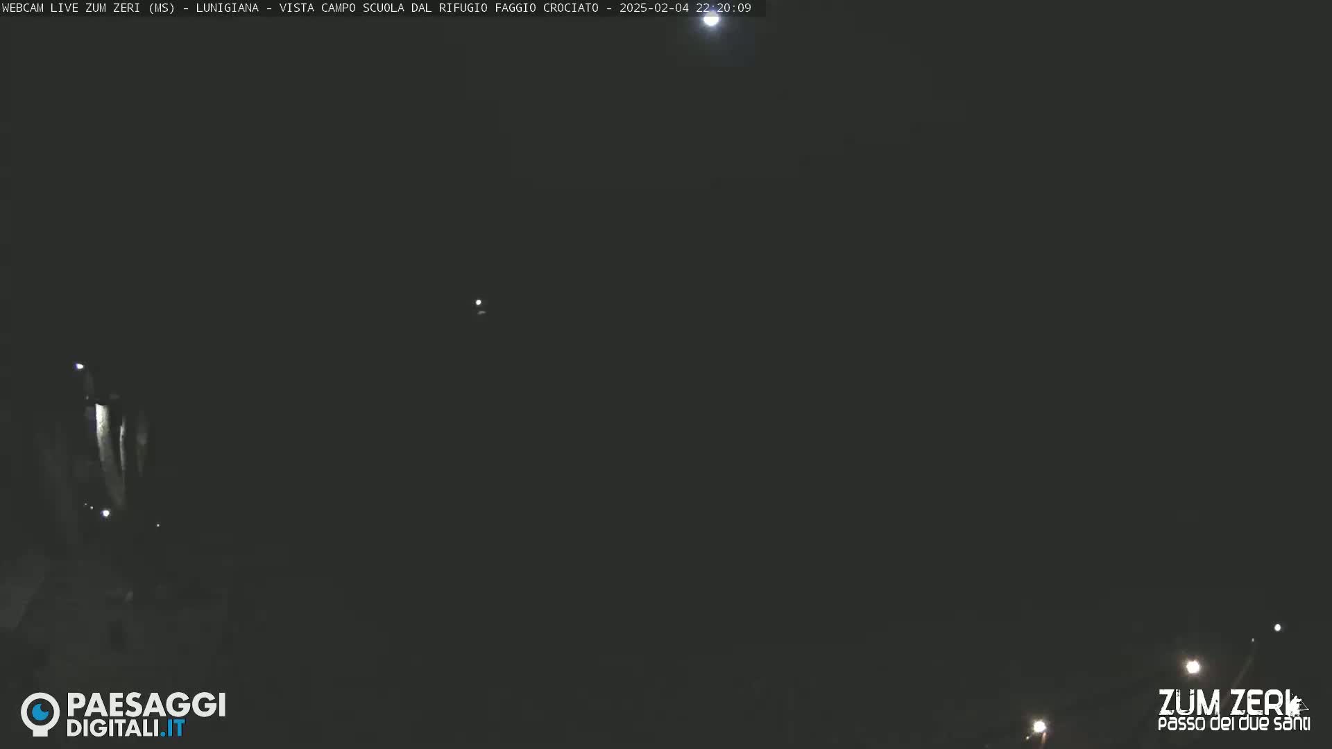 A dark, nighttime scene shows a few faint lights in the distance under a mostly clear sky.