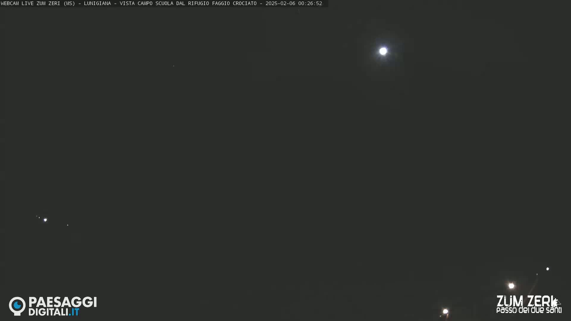 A nighttime image shows a bright moon and several dim lights in a dark sky.