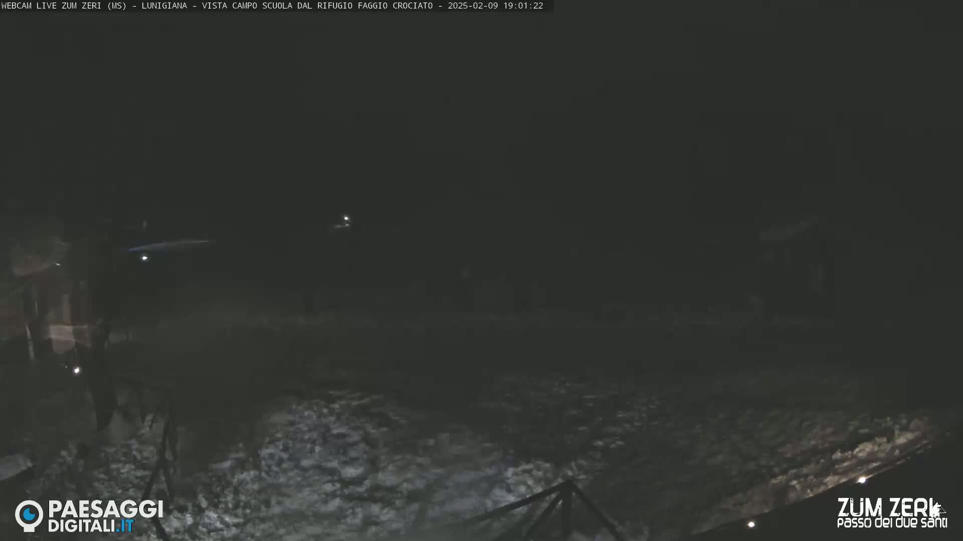 A dark, snow-covered ground is visible at night, illuminated by faint lights in the distance.