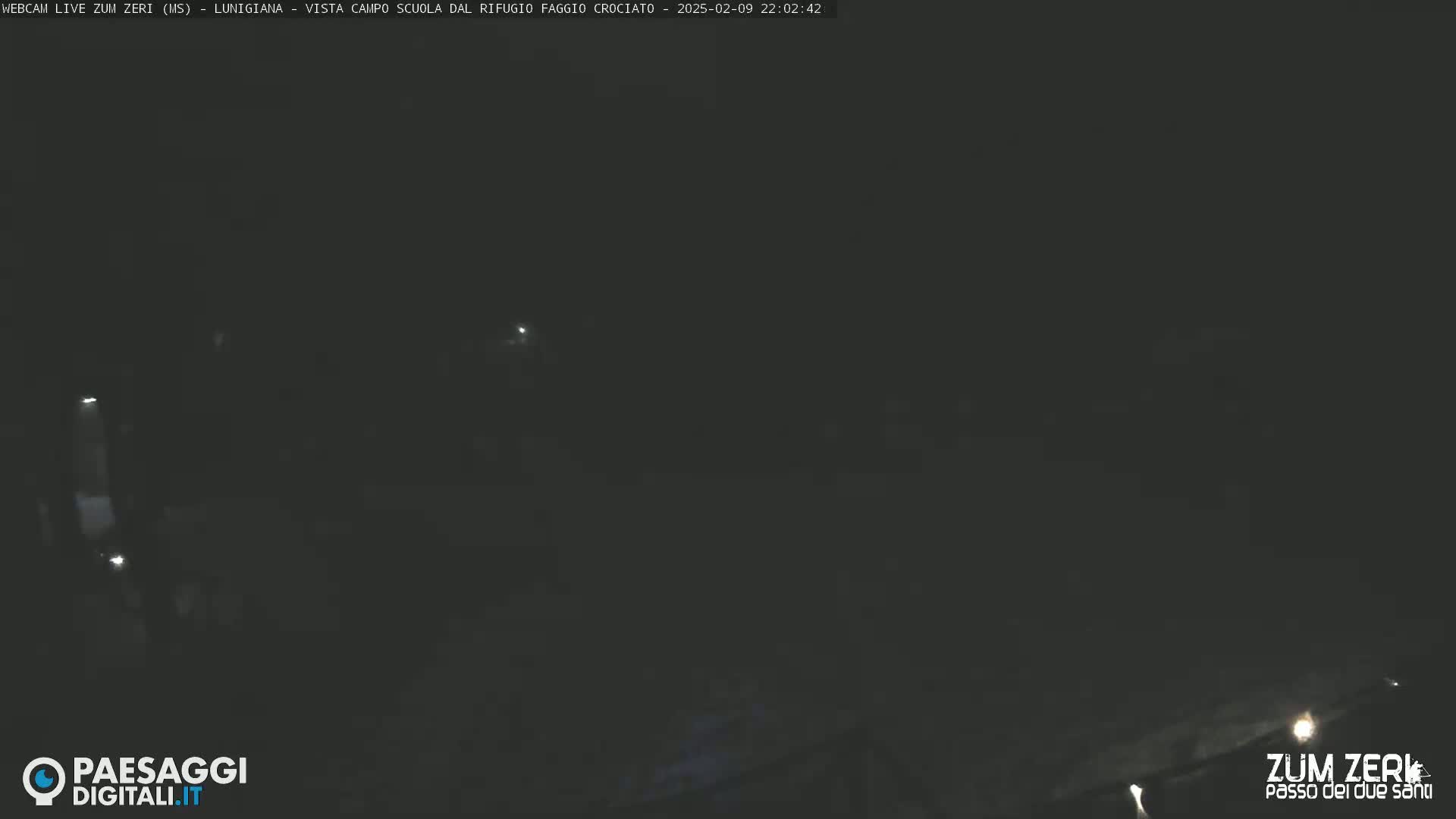 A dark, nighttime scene is shown with a few faint lights visible in the distance.