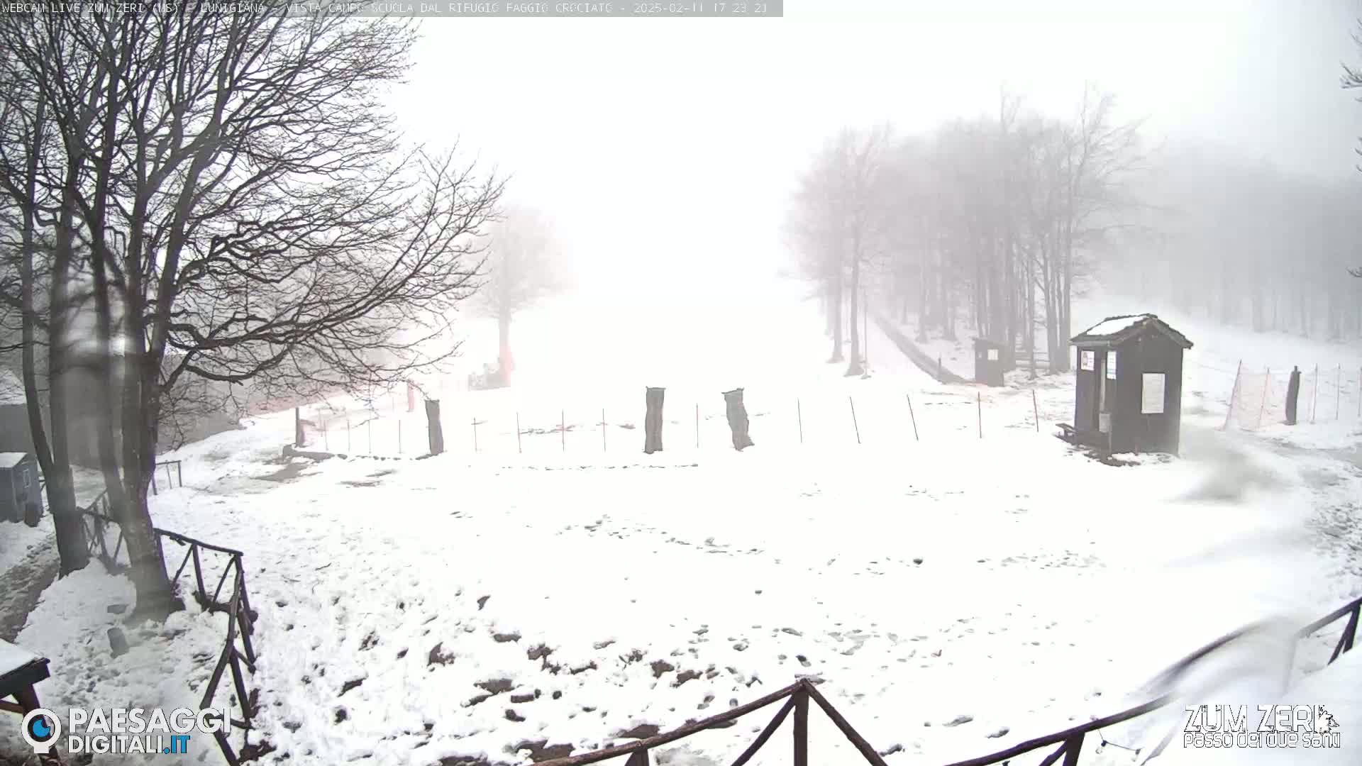 A snow-covered landscape with bare trees and a small building is visible through a foggy atmosphere.