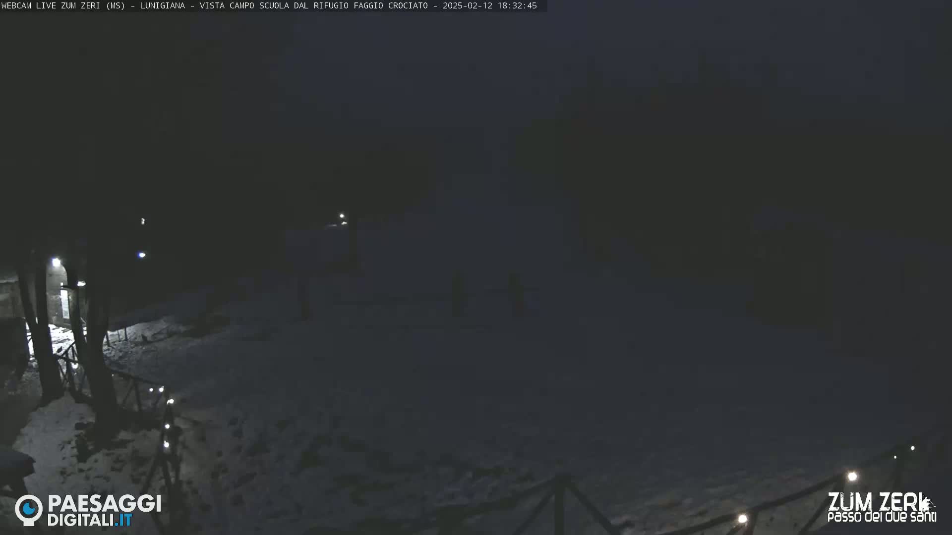 A snow-covered, dimly lit outdoor area at night, with a few faint lights visible in the distance.