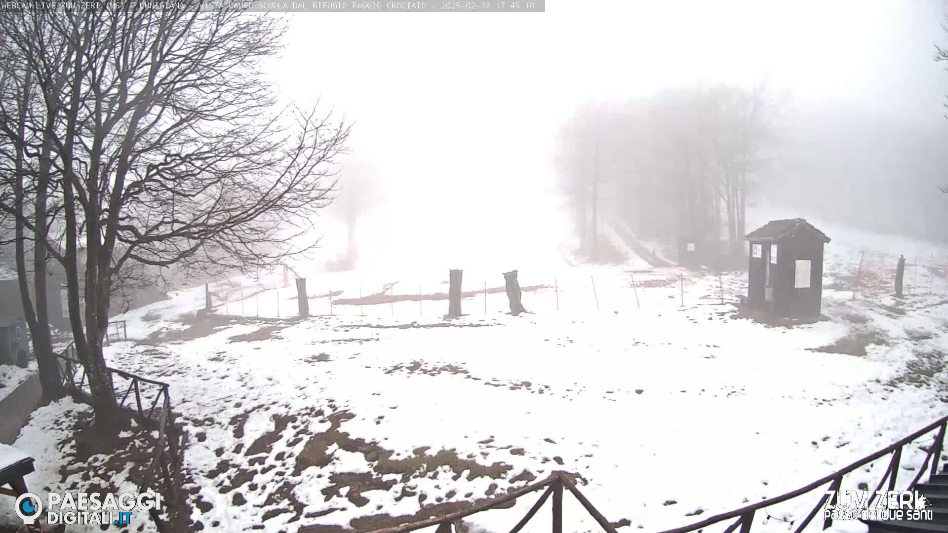 A snow-covered, foggy landscape features bare trees, a small wooden structure, and a wooden fence.