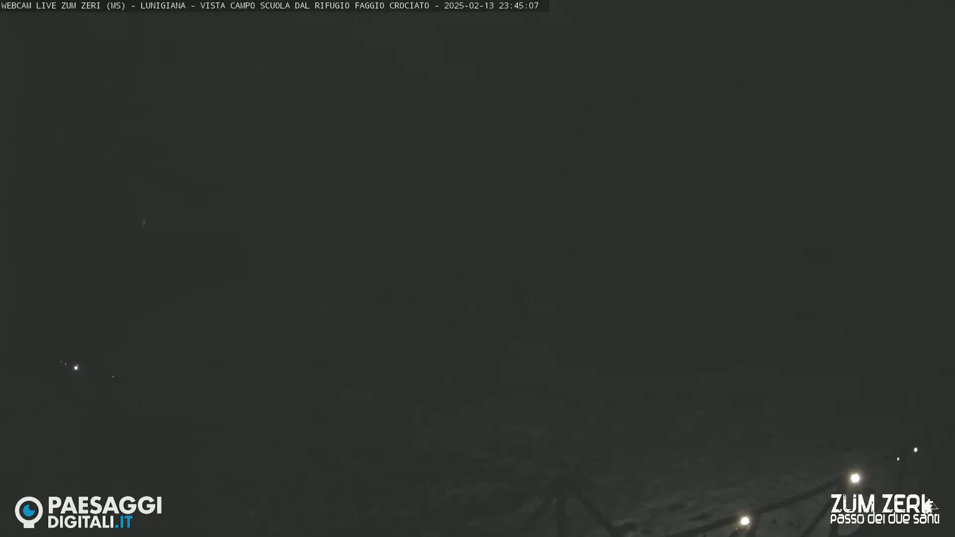 A dark, nighttime outdoor scene shows a snowy ground with a few faint lights in the distance.
