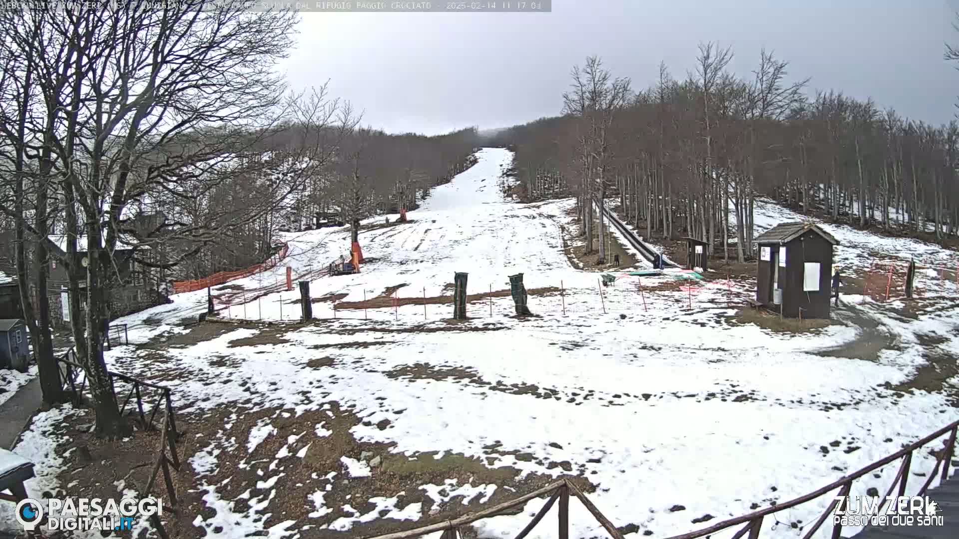 A snow-covered ski slope in a forest under an overcast sky.