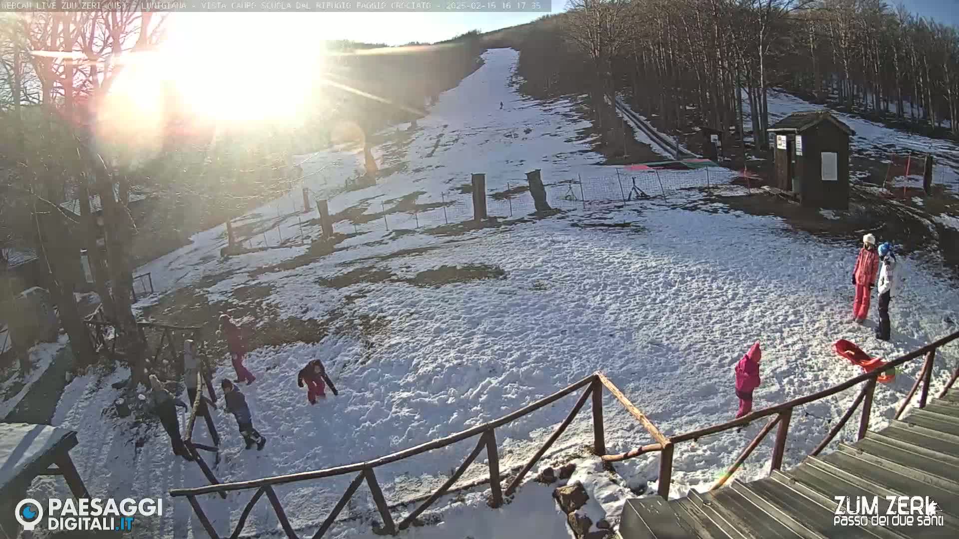 A snow-covered hillside with several children playing in the snow on a sunny day.