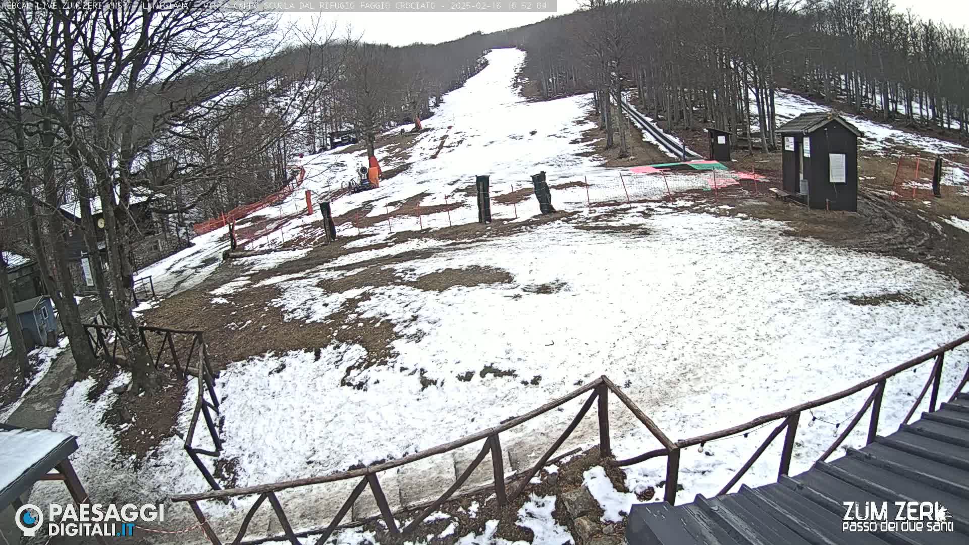 A snow-dusted ski slope with a small building and wooden fence is visible, under a cloudy sky.