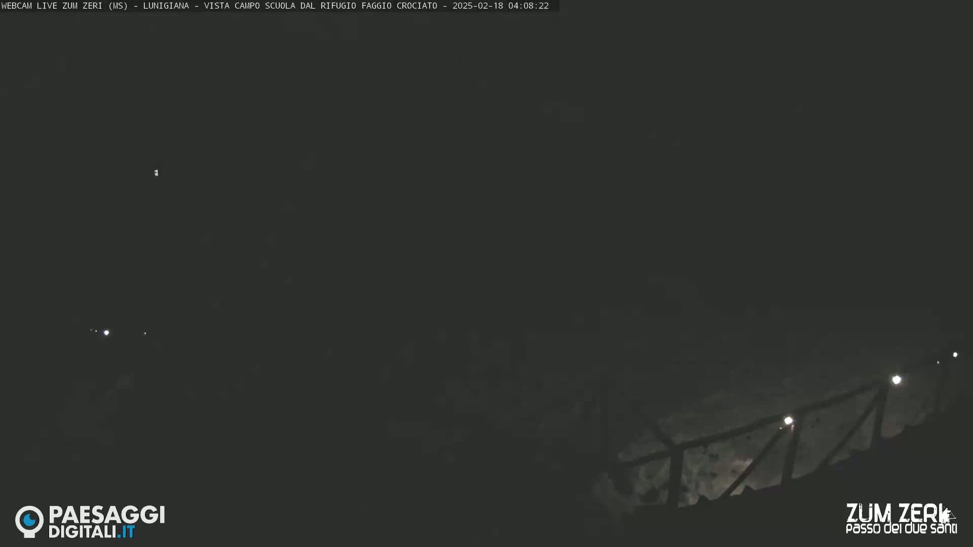 A nighttime, dark outdoor scene shows a dimly lit railing ascending a hill.