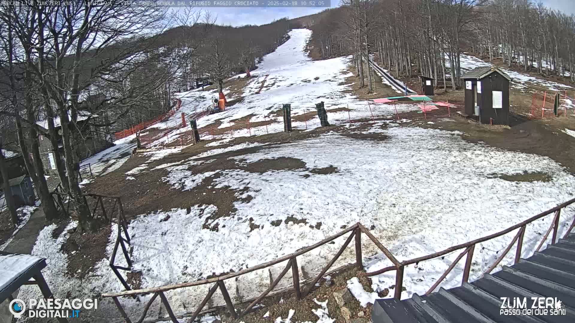 A snow-dusted ski slope with small buildings and a wooden fence is visible under a sunny sky.