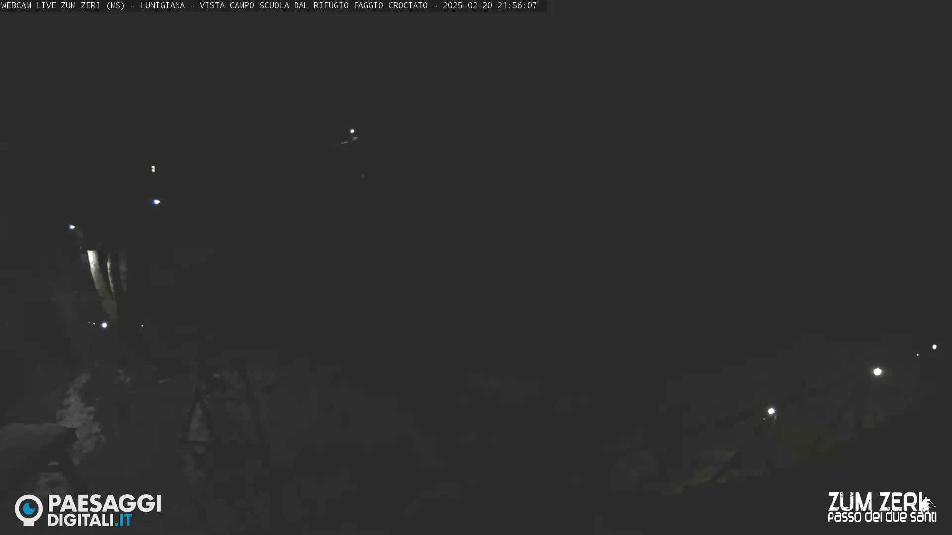A nighttime, dark outdoor scene shows a few faint lights in the distance.