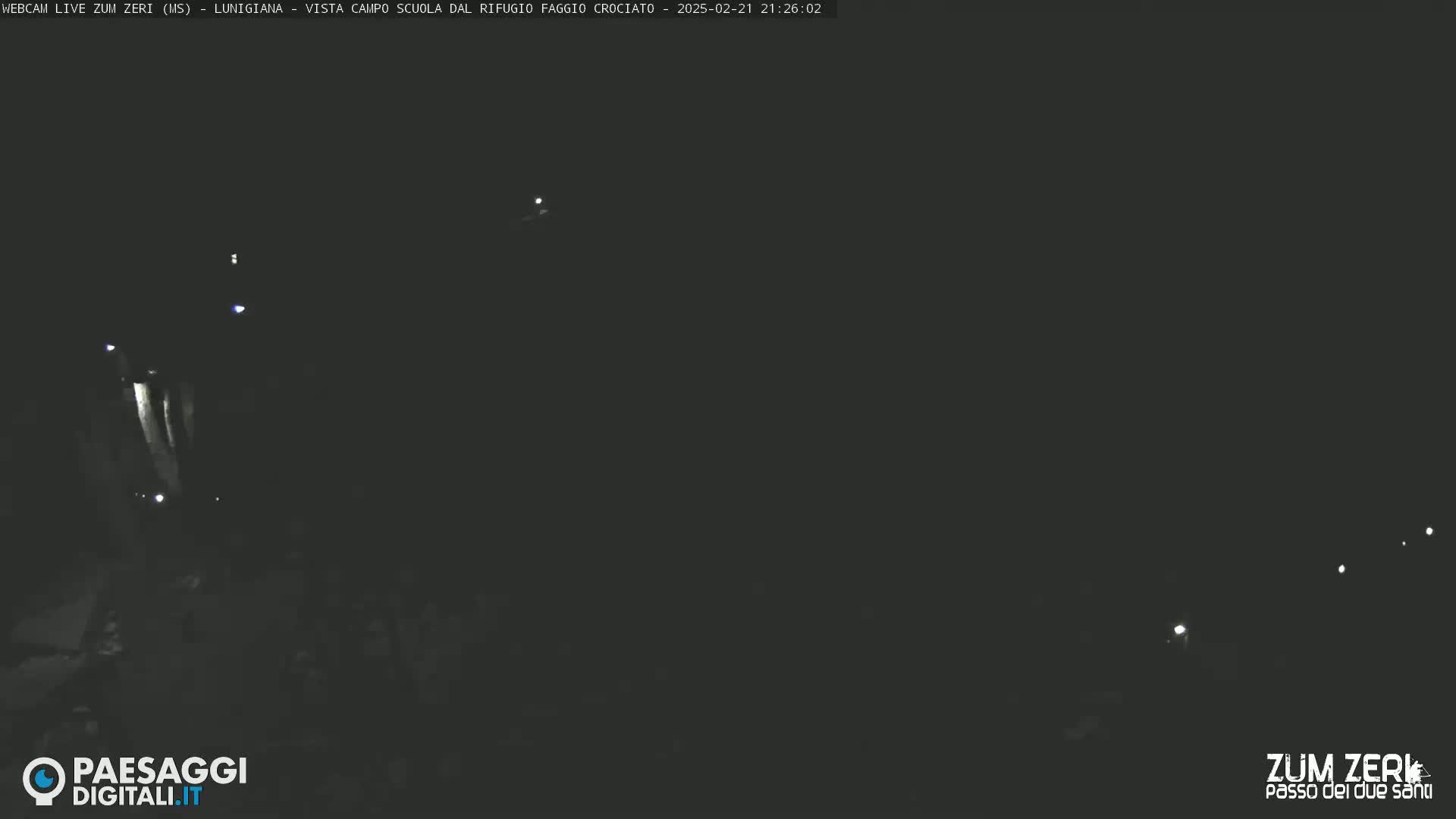 A nighttime, low-light view of a dimly lit area, possibly a road, with a few faint lights visible in the distance.