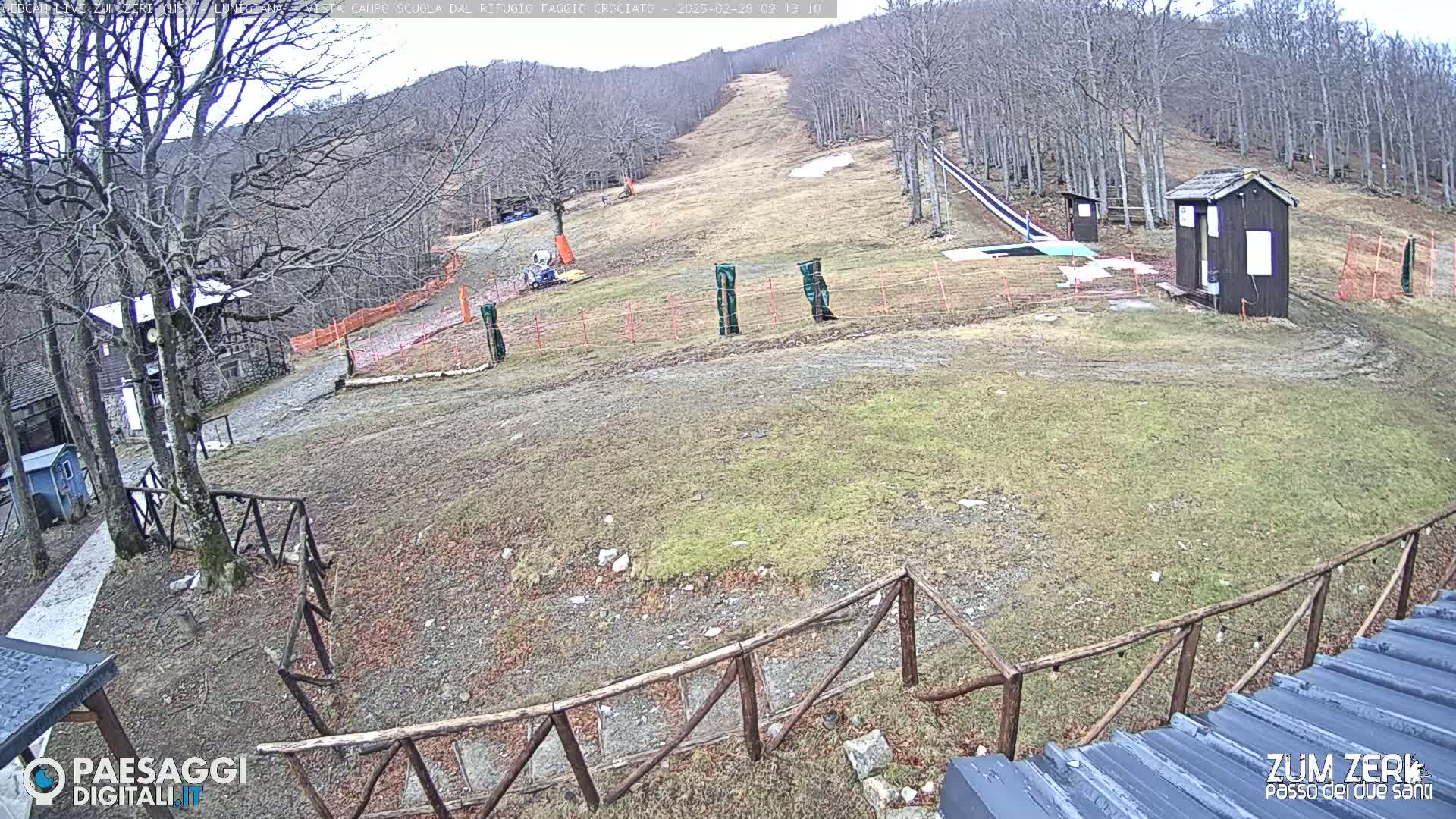 A mostly barren ski slope is visible, with a few small buildings and fences near the bottom, under an overcast sky.