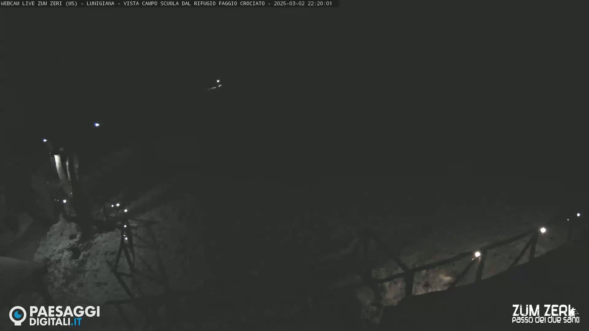 A nighttime, snow-covered landscape is dimly lit by several small lights along a railing.
