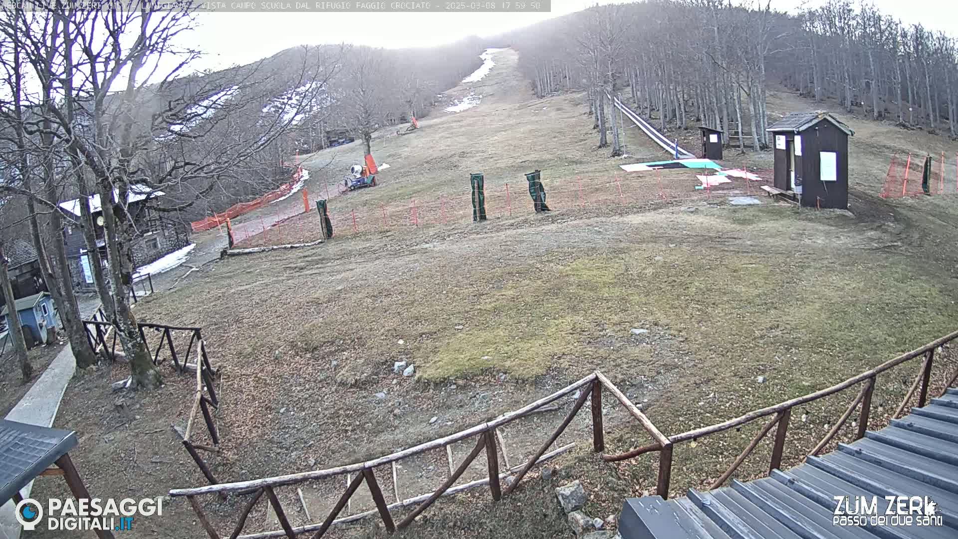 A mostly barren, grassy hillside with a small wooden building and a ski slope under a cloudy sky.