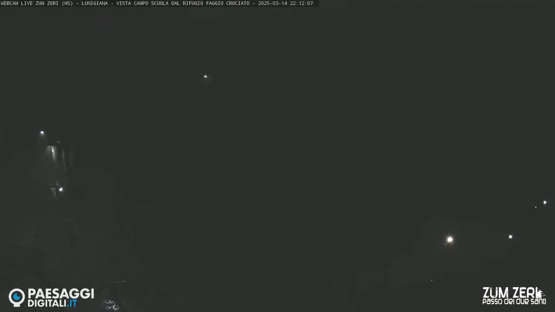 A dark nighttime scene shows a few distant lights and what appears to be a vehicle's headlights in the lower-left.